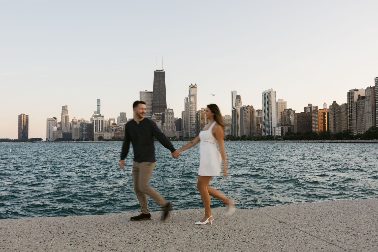 Couple walking along Lake Michigan shoreline with Chicago's iconic skyline in the background.