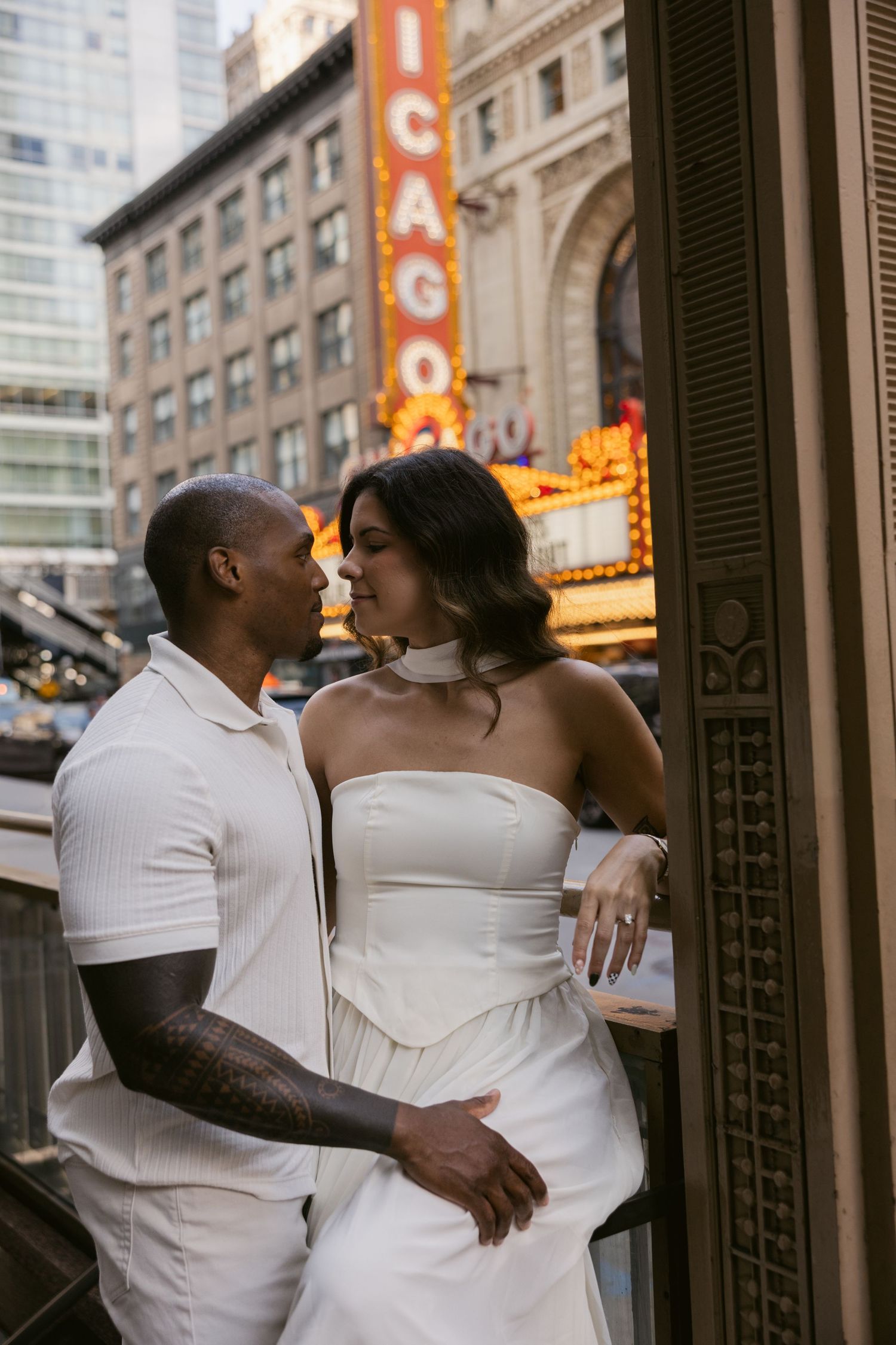 Intimate moment captured between a couple in white attire against an urban backdrop with vintage signage.