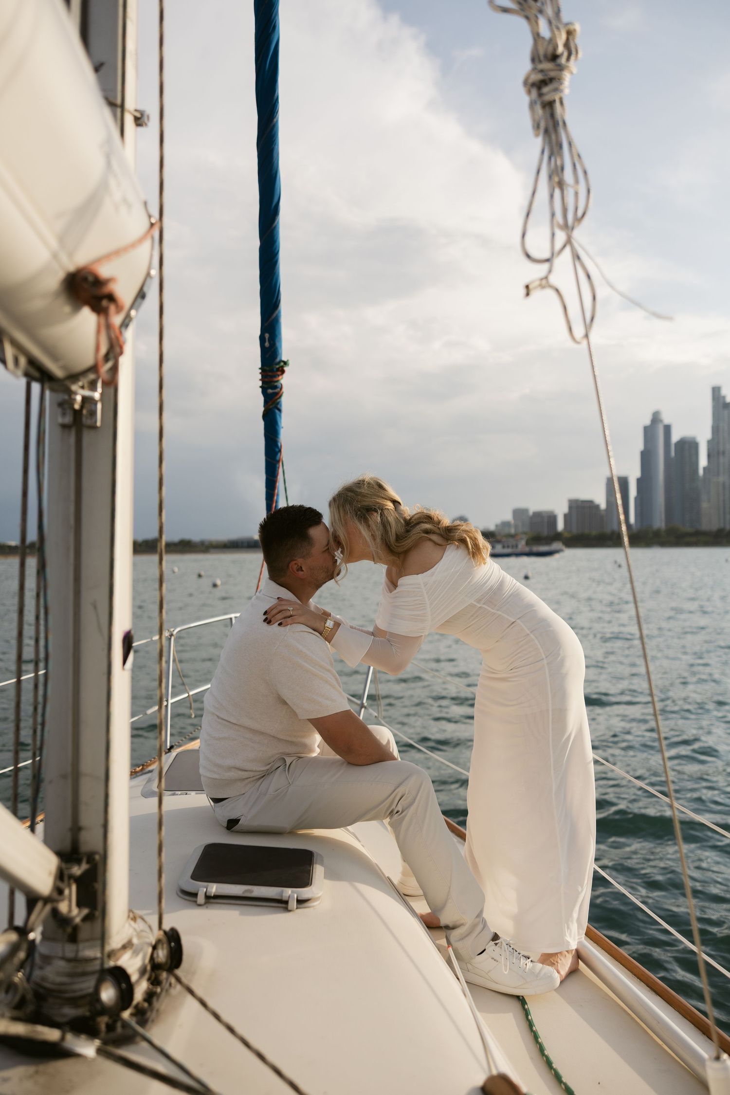 Couple in white clothing sharing an intimate moment on a sailboat with city skyline visible in the background.