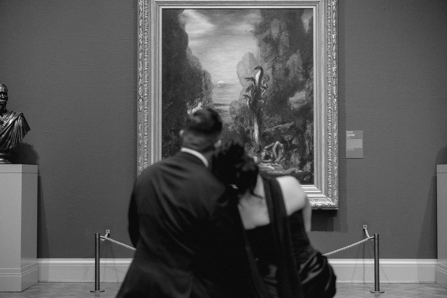 Gold-framed artwork hangs on dark gray walls in an elegant museum gallery.