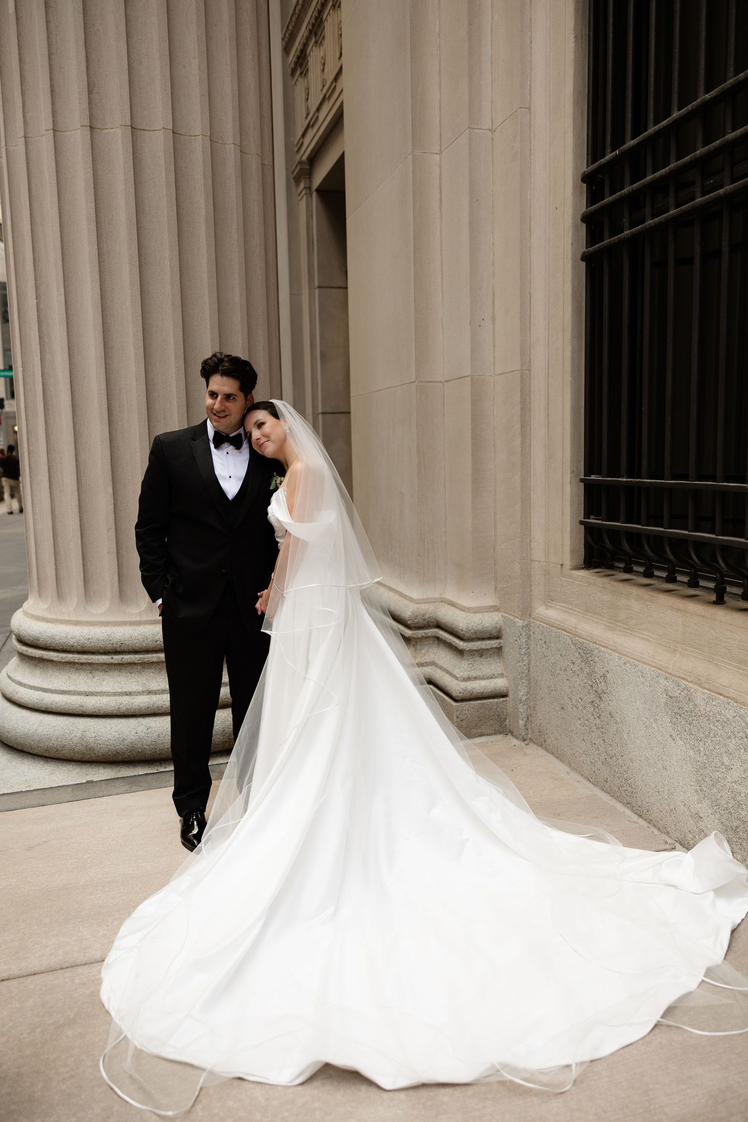 A dramatic wedding portrait against classic architectural columns with a flowing white dress train.