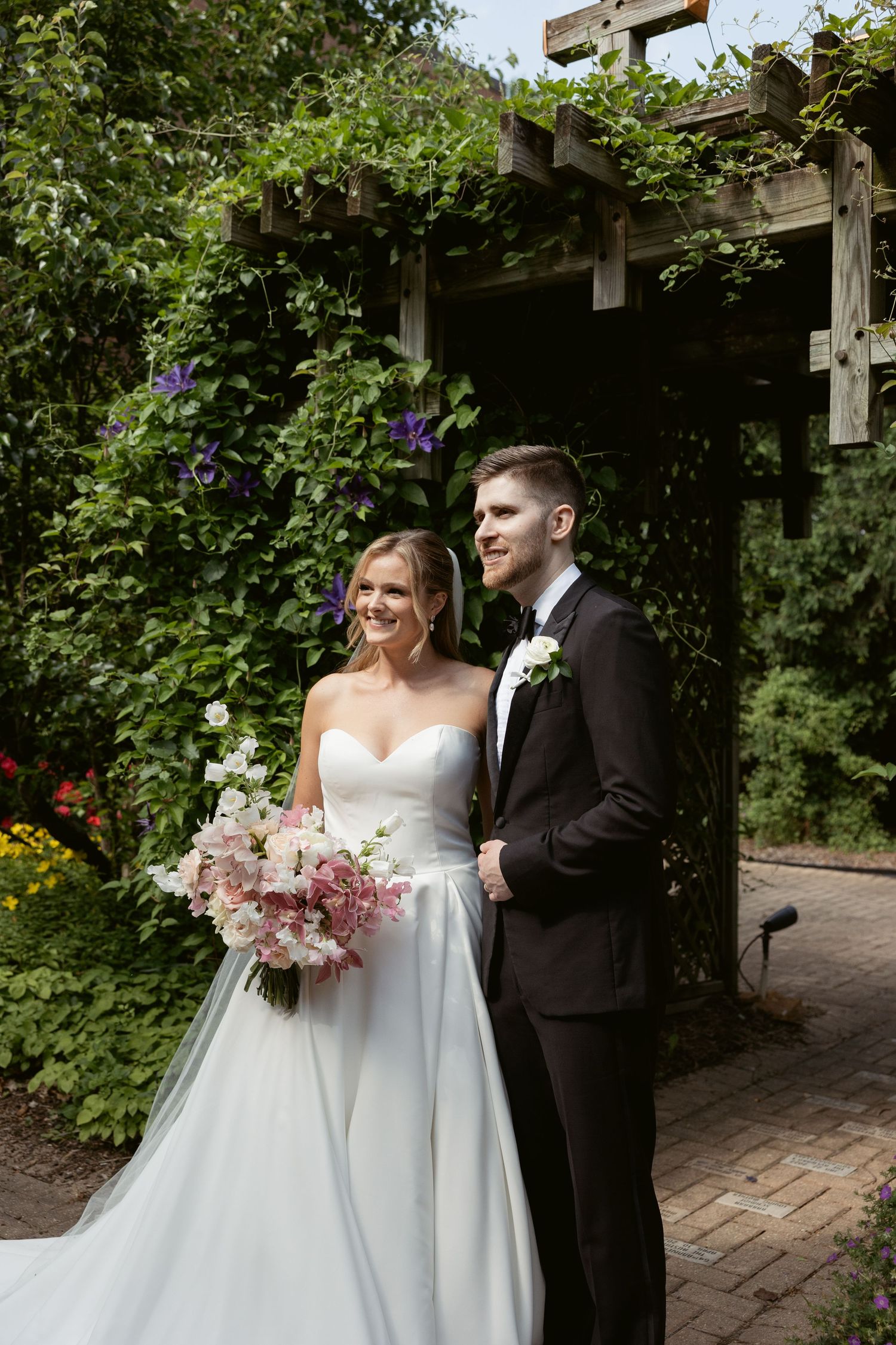 Wedding couple shares intimate moments under a wooden arbor surrounded by lush garden greenery.