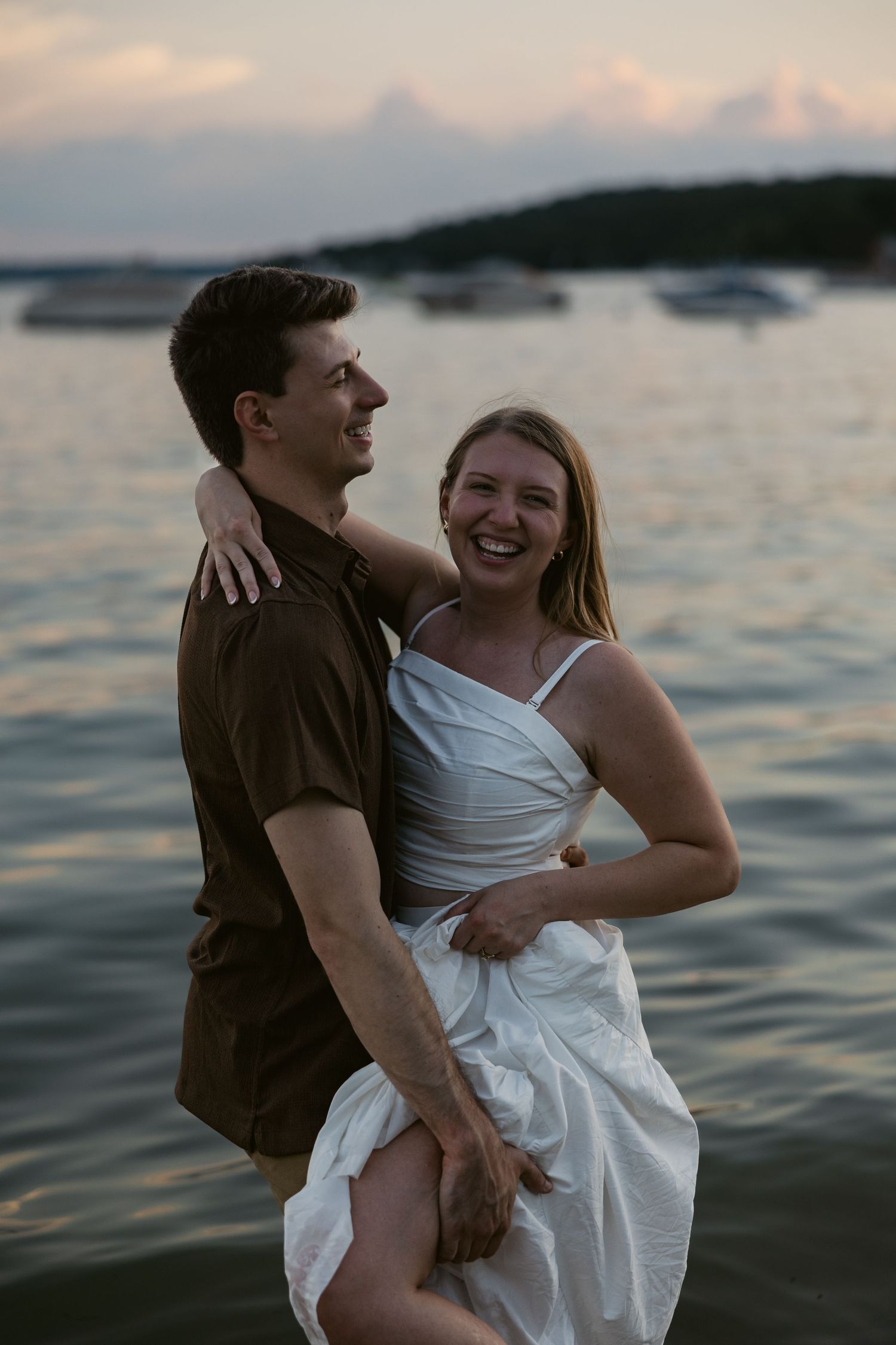 A candid moment of laughter and embrace during a lakeside photoshoot at dusk.