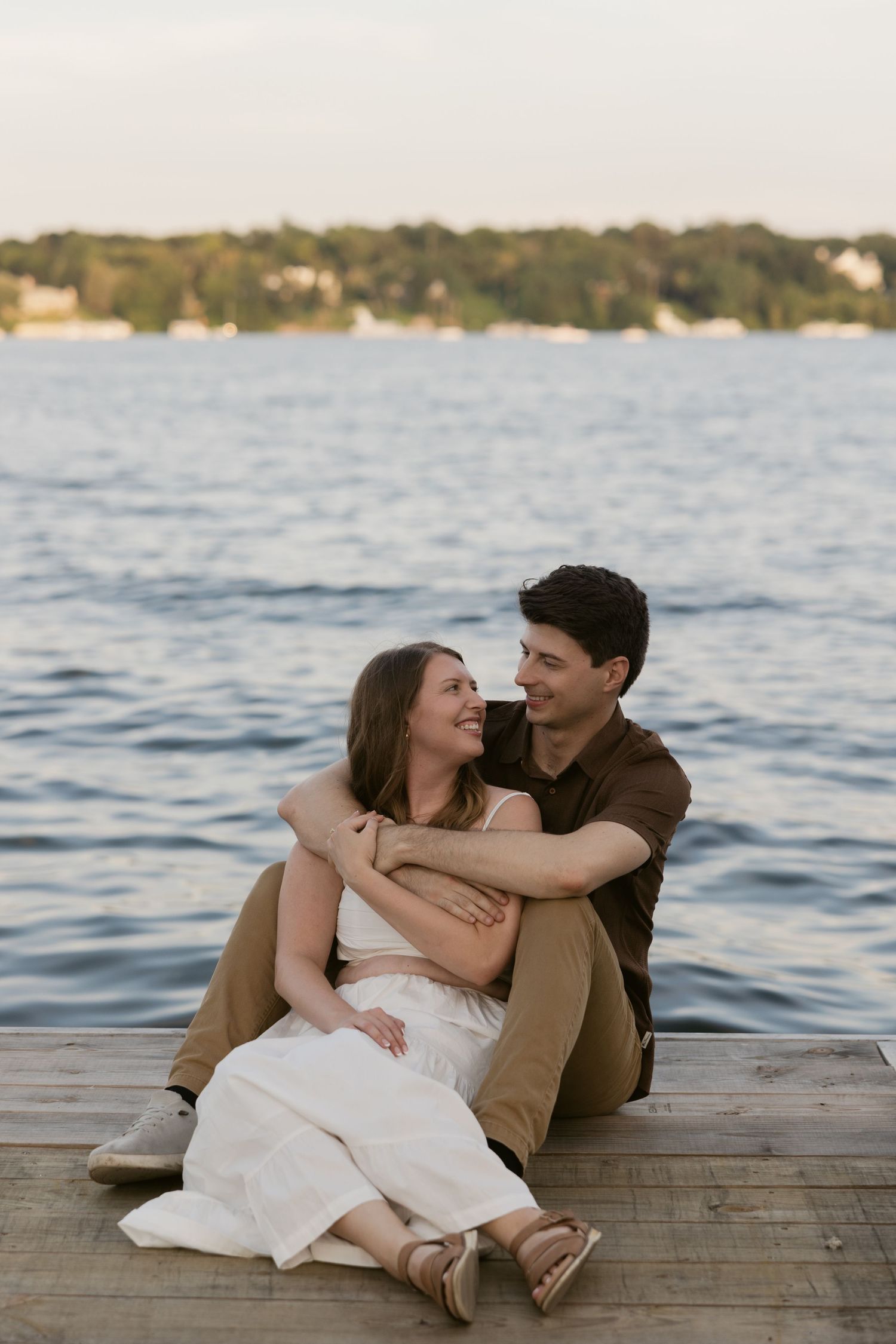 Couple sitting together and embracing on a wooden dock by the lake at sunset.