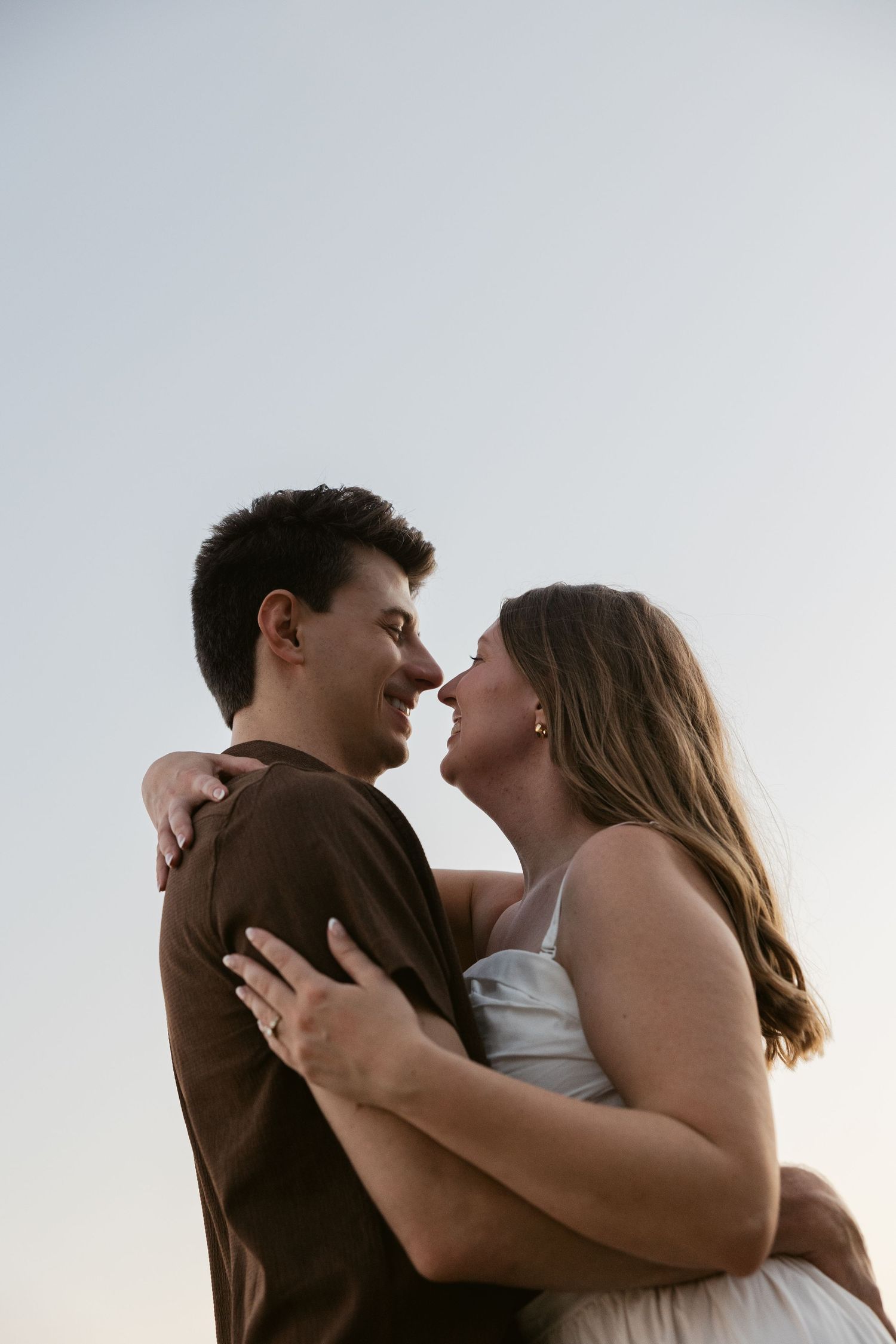 An intimate couple embraces against a bright sky background in a close-up shot.