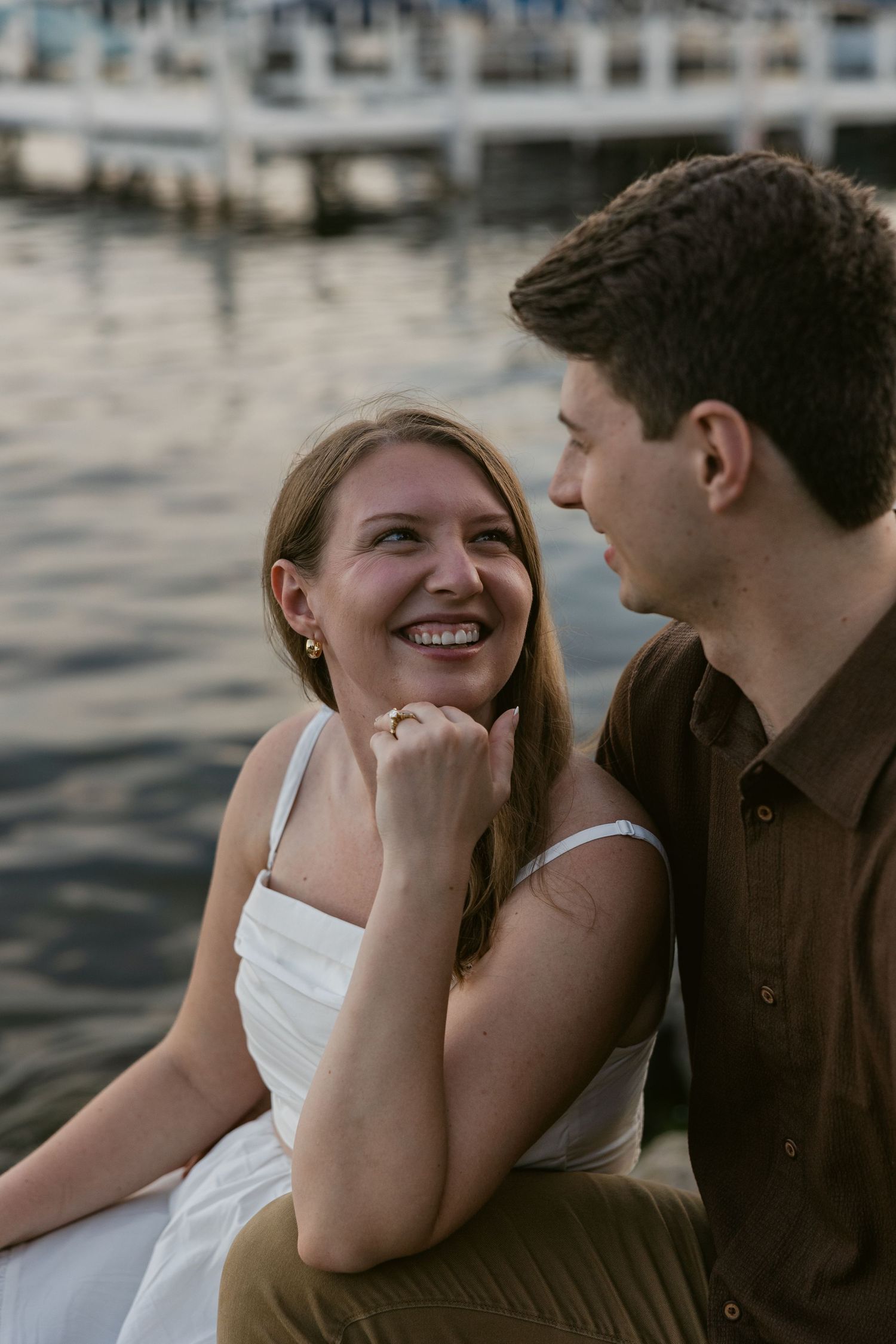 Romantic candid moment of a couple sharing laughter while sitting on a dock at twilight.
