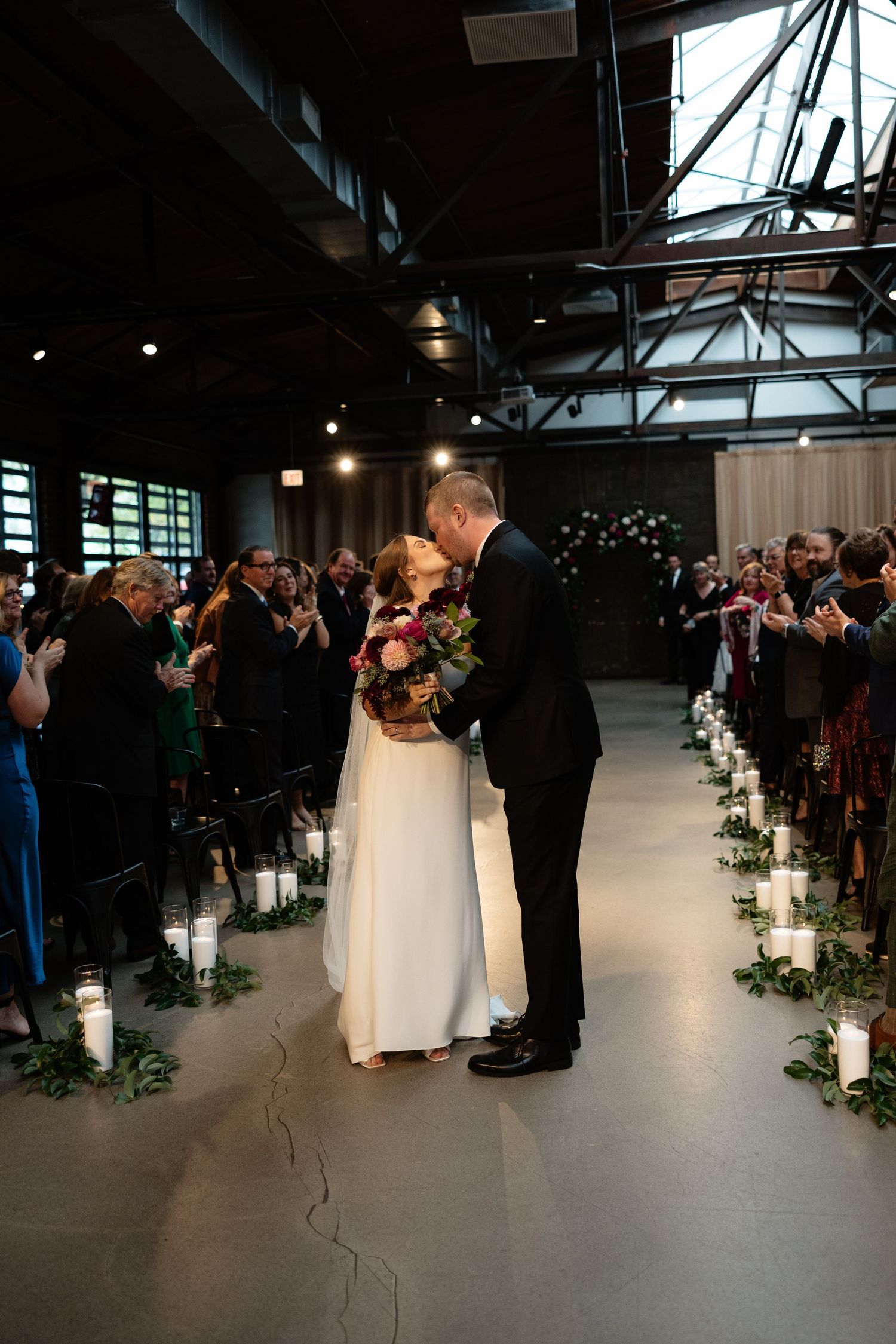 Indoor wedding ceremony in modern industrial venue with ambient lighting and floral decorations.