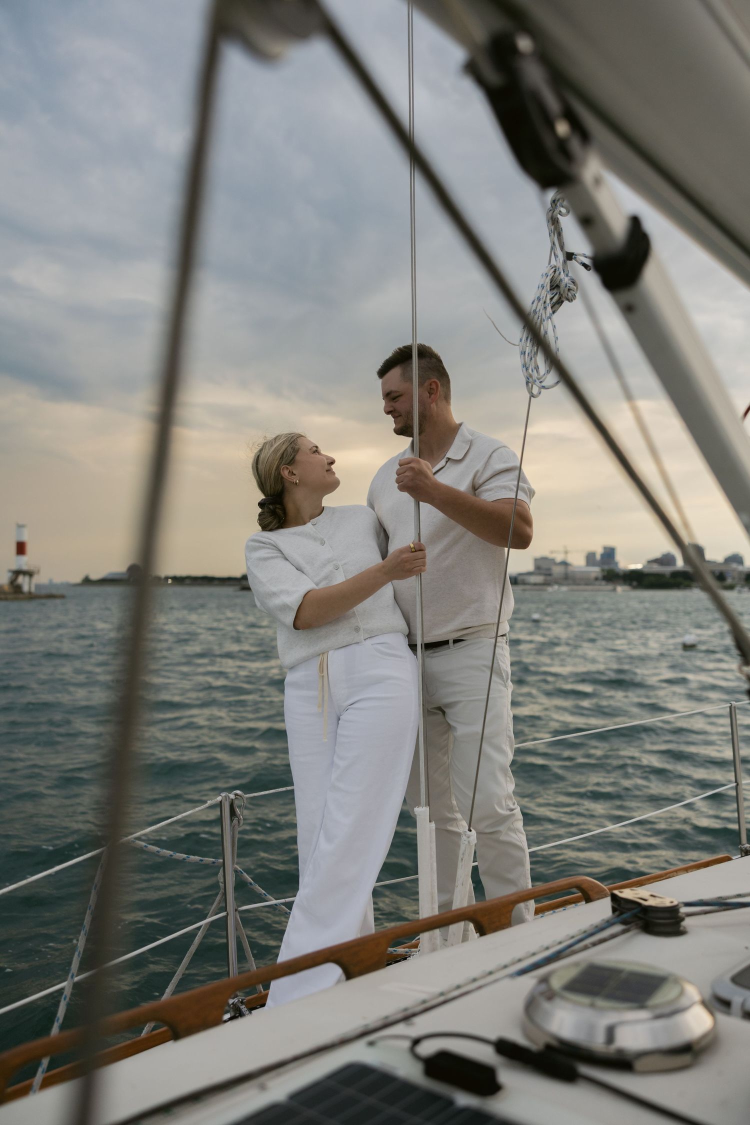 A couple dressed in white embraces on a sailboat deck with nautical equipment visible.