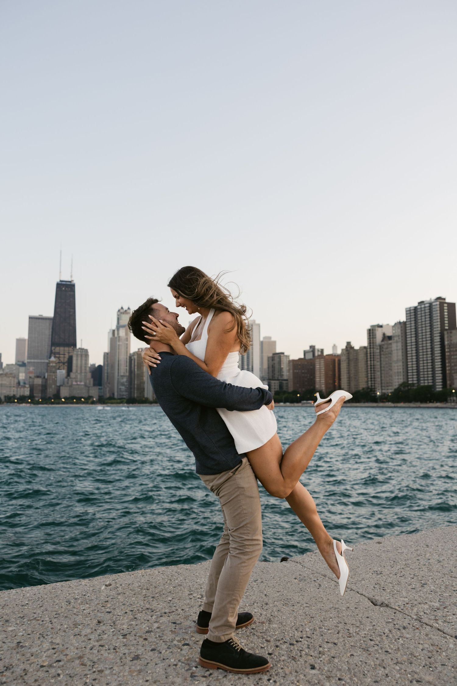 Playful couple sharing intimate moment on Lake Michigan shore with Chicago skyline backdrop.