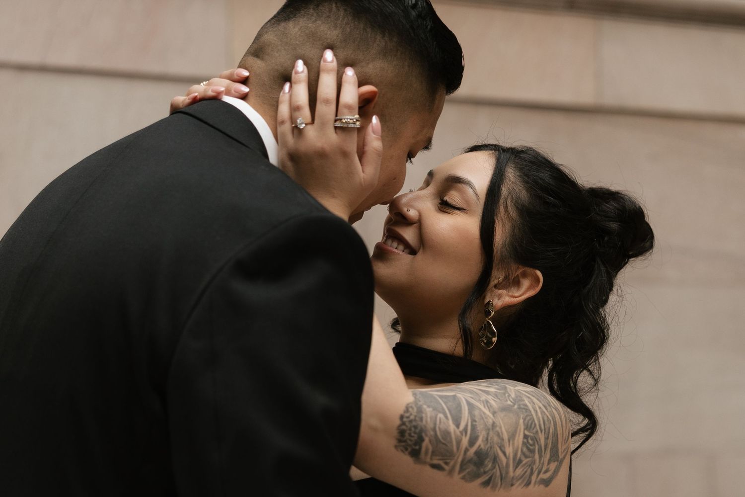 A romantic couple embraces in an intimate moment, with the woman's tattooed arm visible against formal attire.