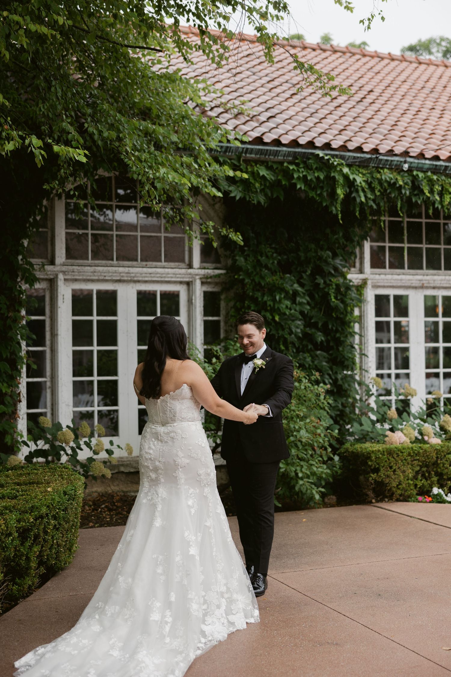 First look wedding moment captured in sequence outside a Spanish-style building with ivy covered walls and clay tile roof.