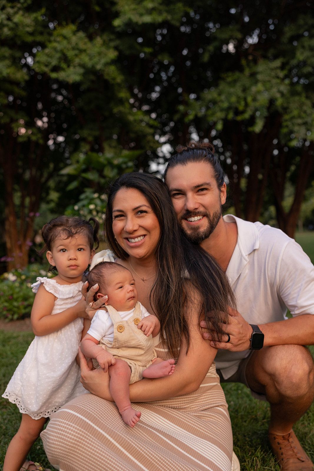 A young family of four poses together outdoors during golden hour.
