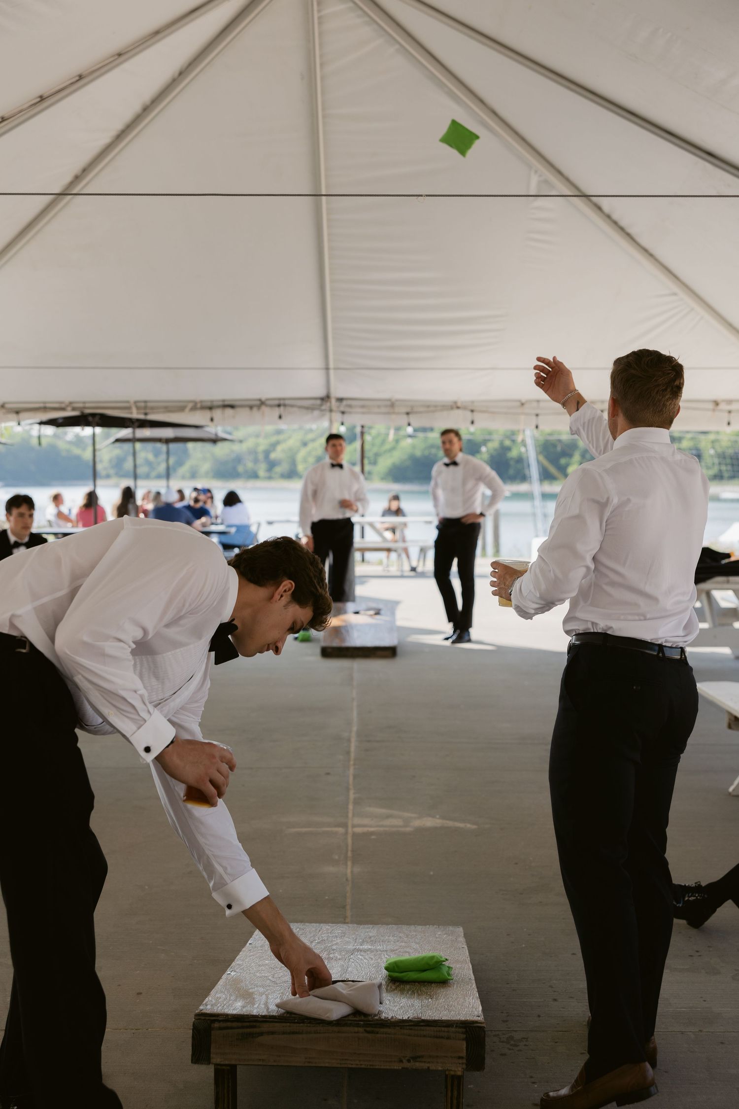 Wedding reception staff members flip and rotate tables in preparation under a large white tent.