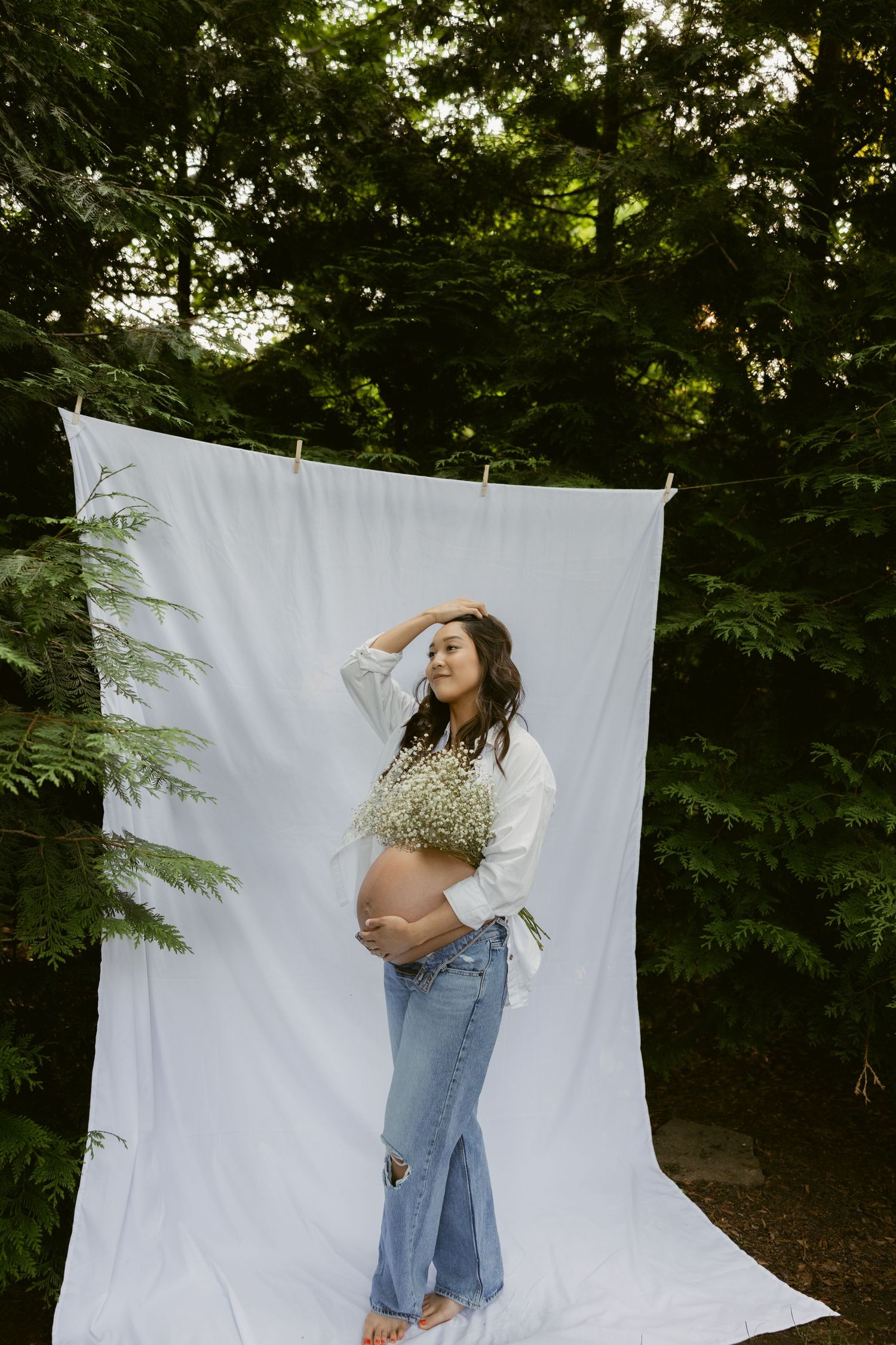 Artistic maternity portraits against white backdrop with green foliage in background.