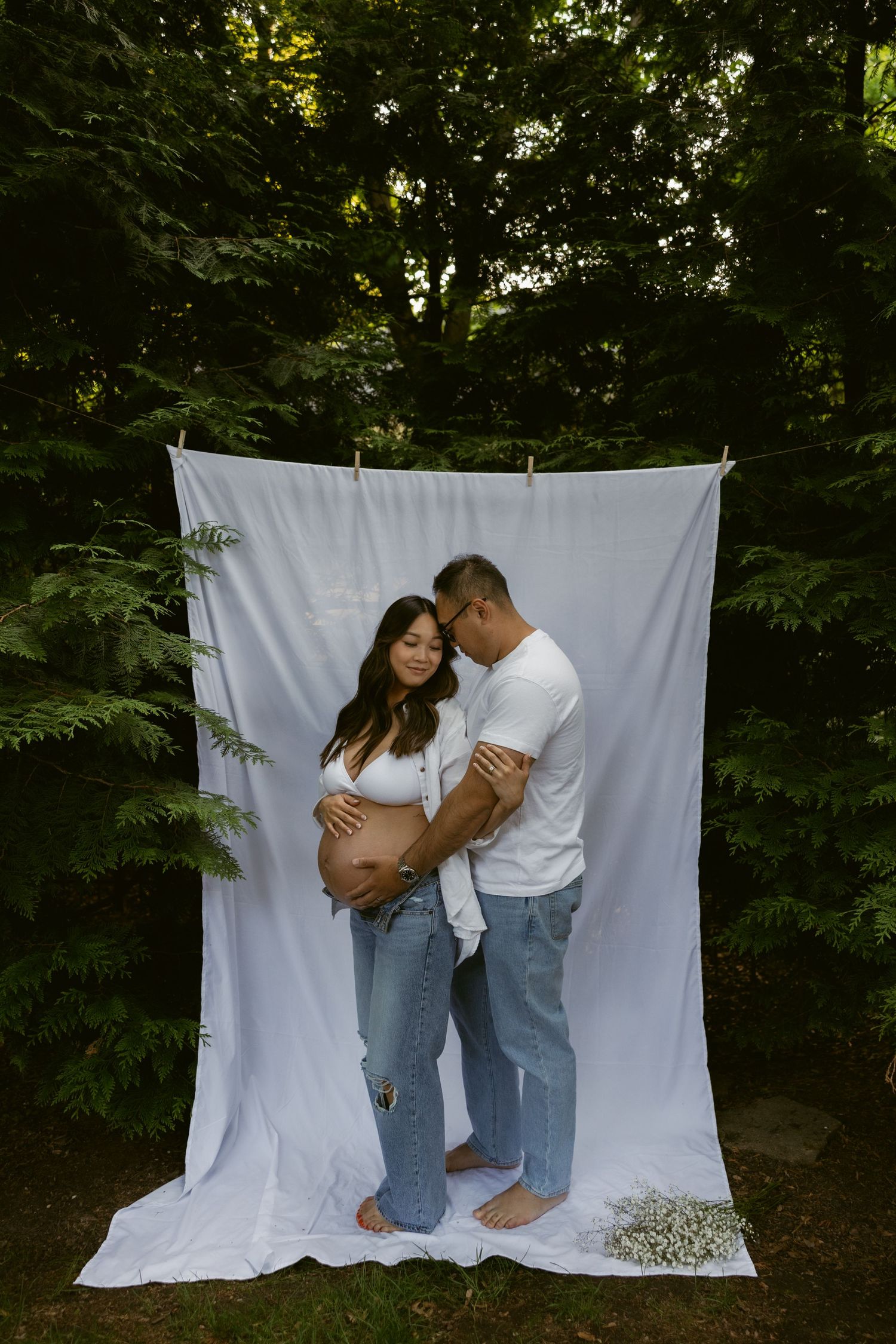 An intimate pregnancy photoshoot with a couple in matching denim and white outfits.