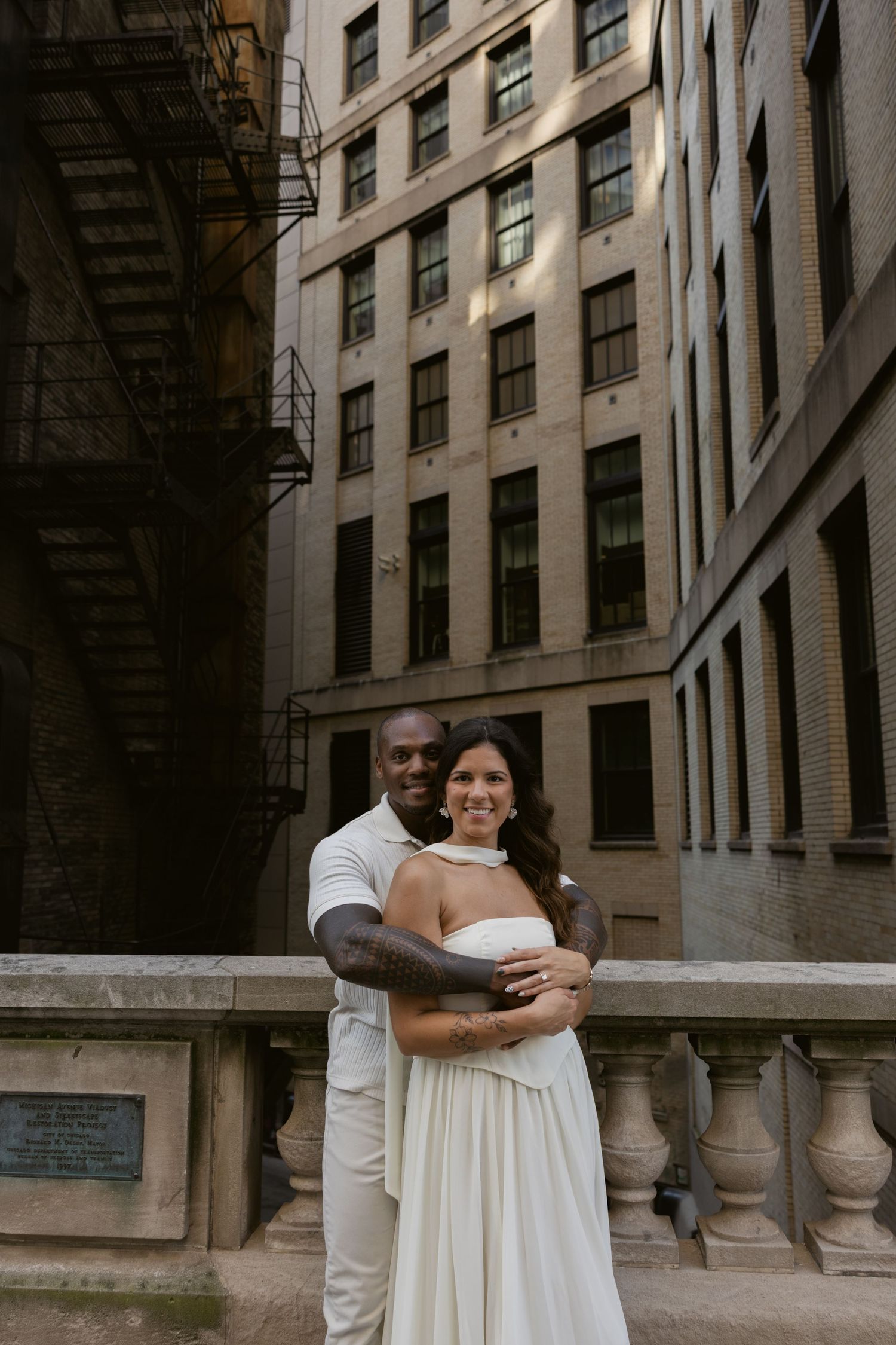 Couple embraces in front of an ornate stone building facade in urban setting.