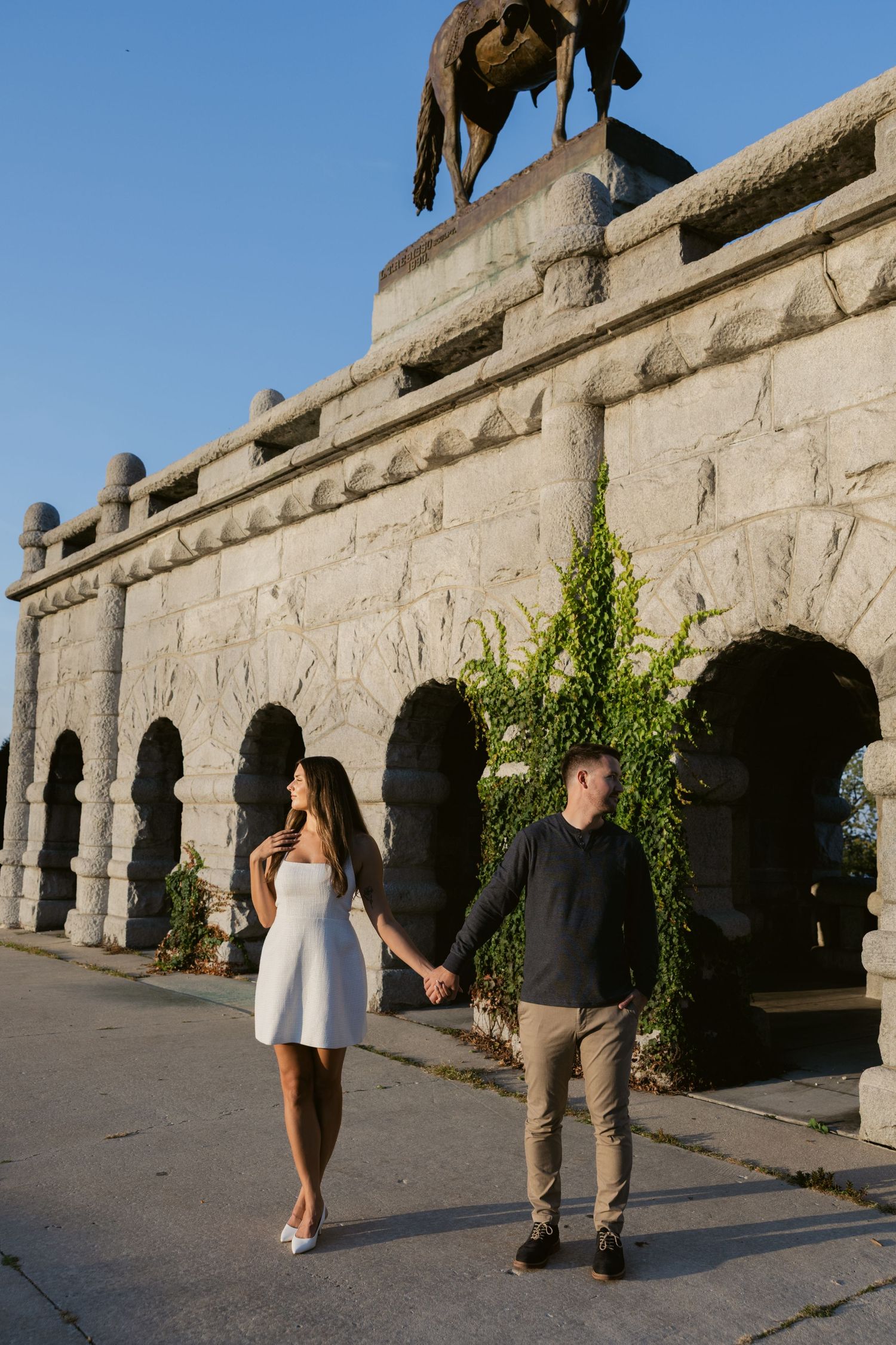 A couple walks along a historic stone colonnade with arched architecture.