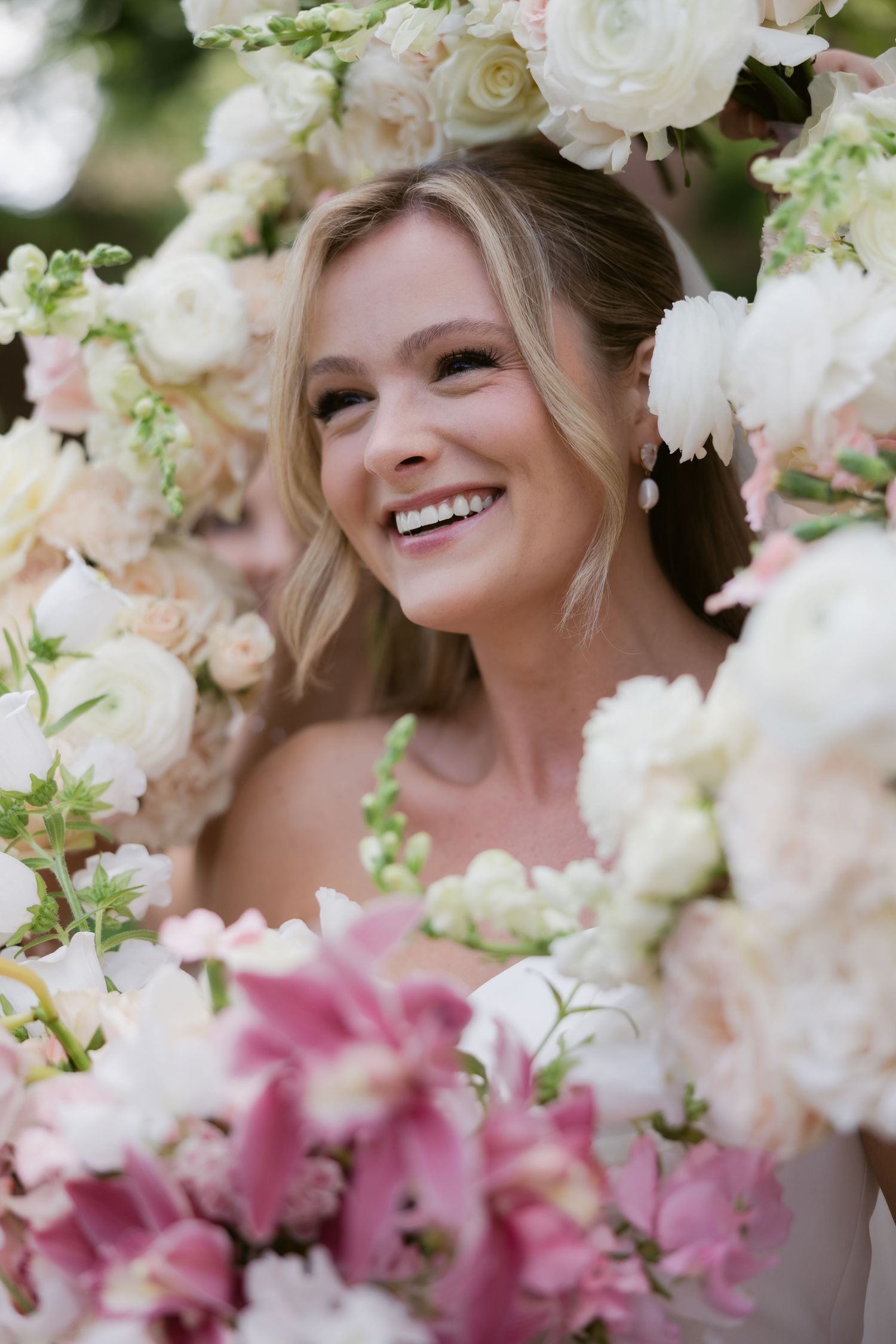 Bride surrounded by white and pink flowers in a romantic garden setting.