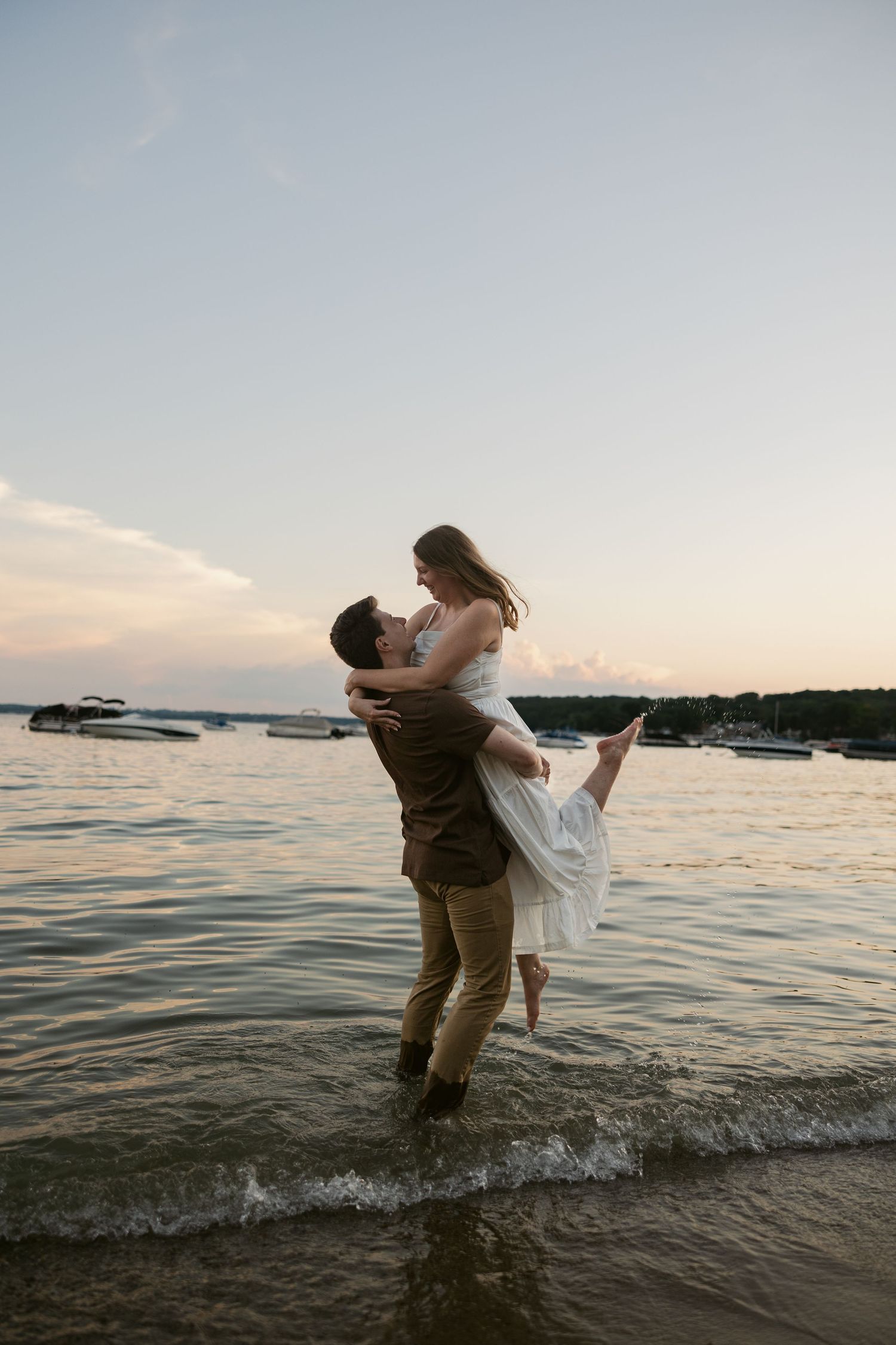 A playful couple splashes in the water at the beach during sunset.