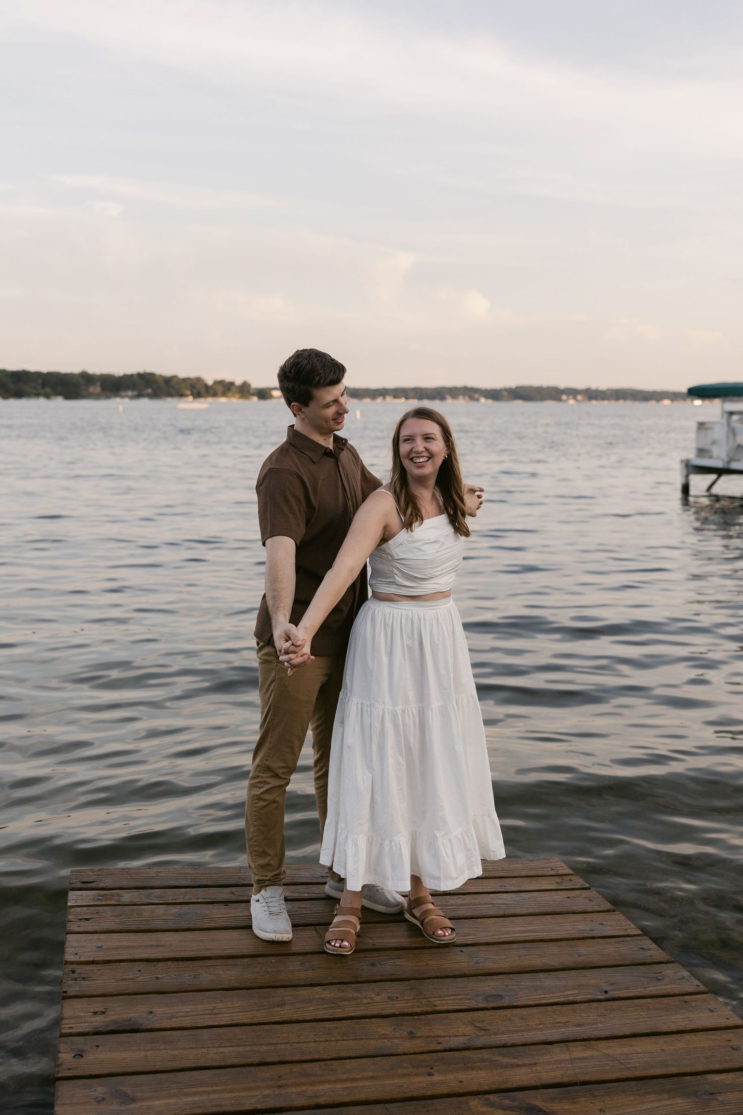 A couple stands together on a wooden dock overlooking a serene lake at dusk.