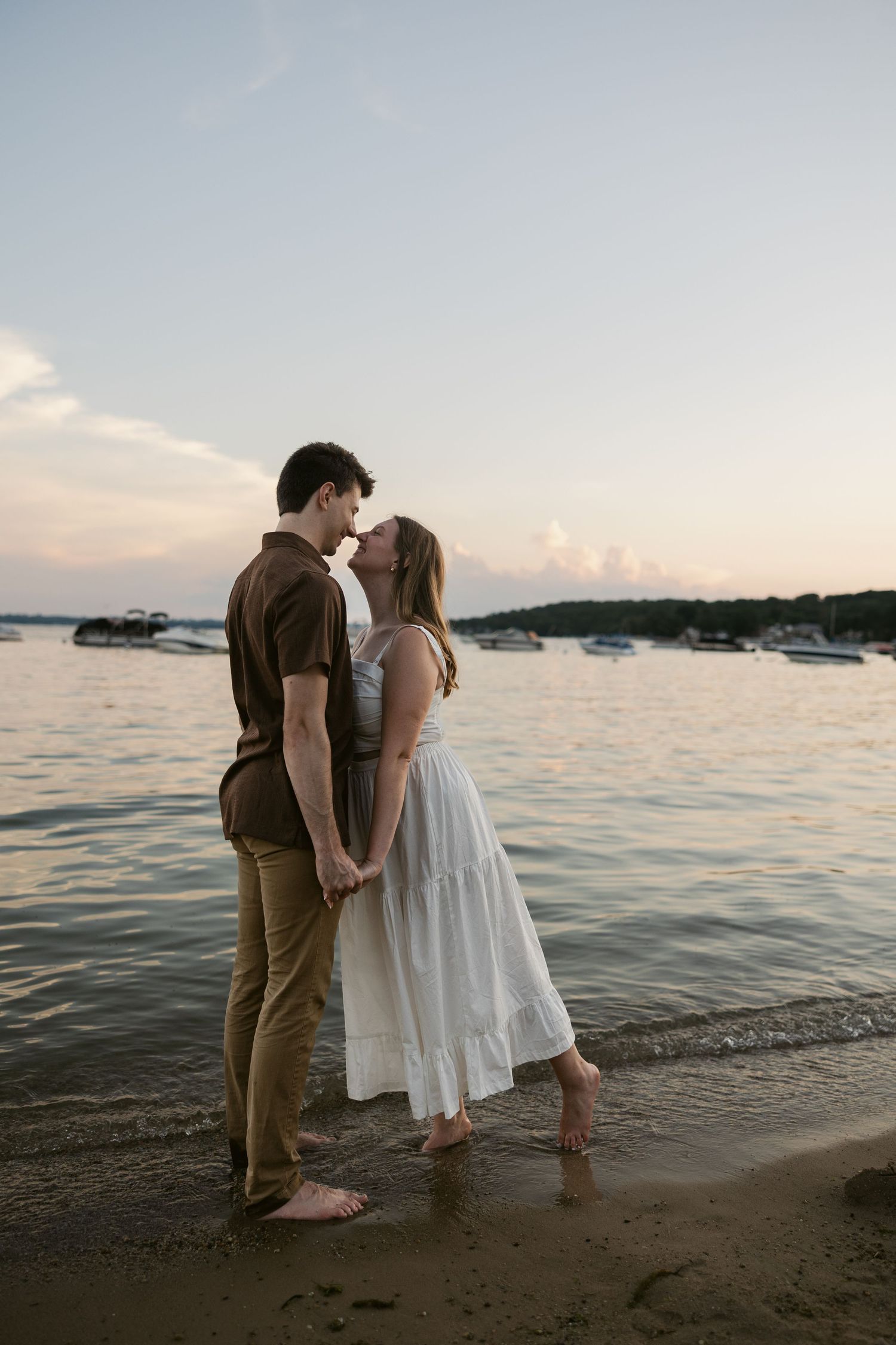 Romantic beach photo shoot at sunset with couple standing in the shallow ocean waters.