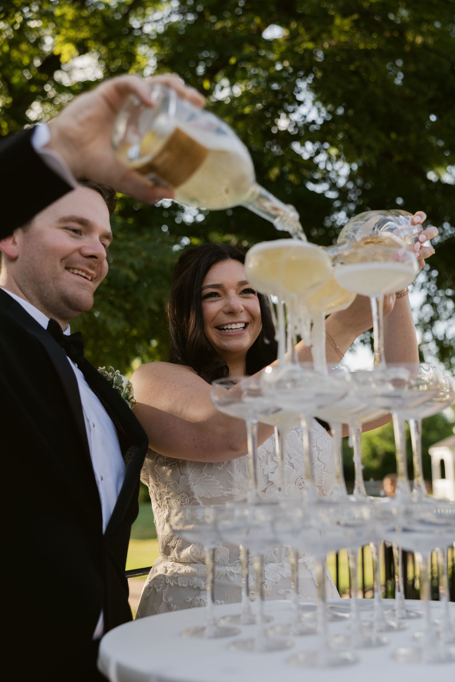 Champagne tower being filled with sparkling wine at an elegant outdoor wedding reception.