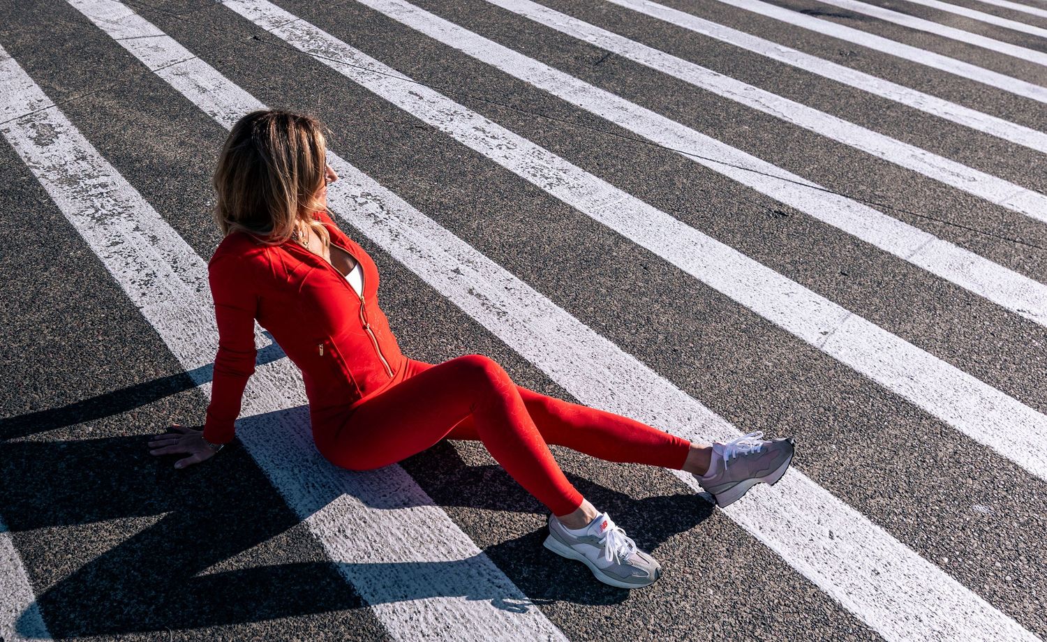 Woman in red athletic wear sitting on striped pedestrian crosswalk outdoors.