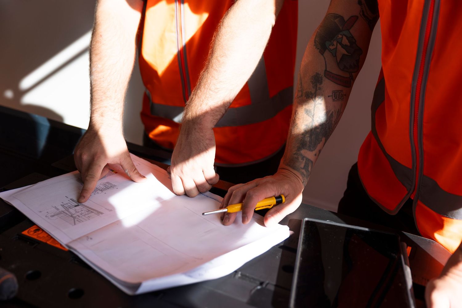 Two construction workers in hi-vis vests reviewing blueprints together on a worksite.
