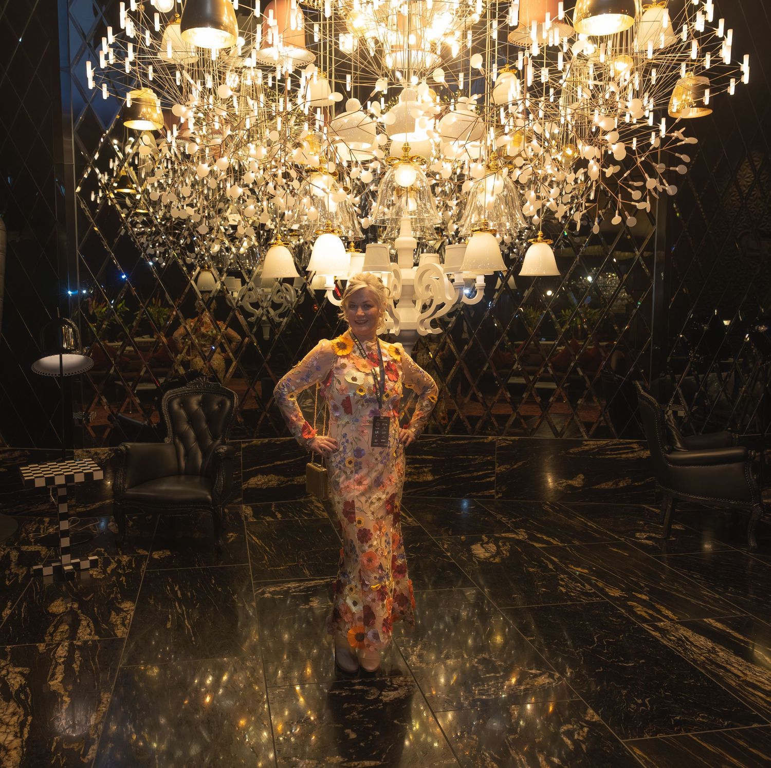 Elegant woman in floral gown posing beneath grand crystal chandeliers in a luxurious mirrored interior.