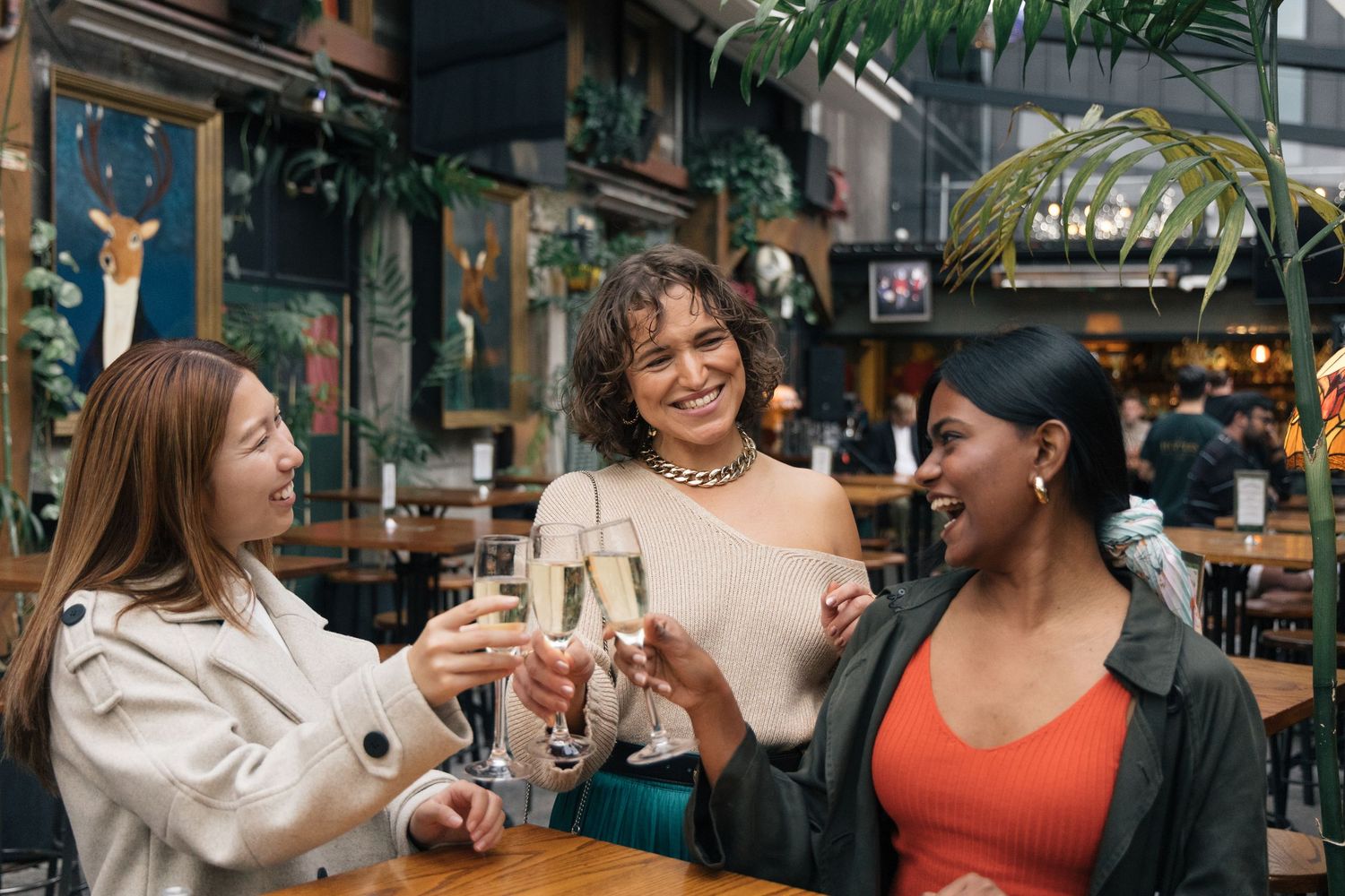 Three diverse women smiling and toasting with champagne glasses at a restaurant table.