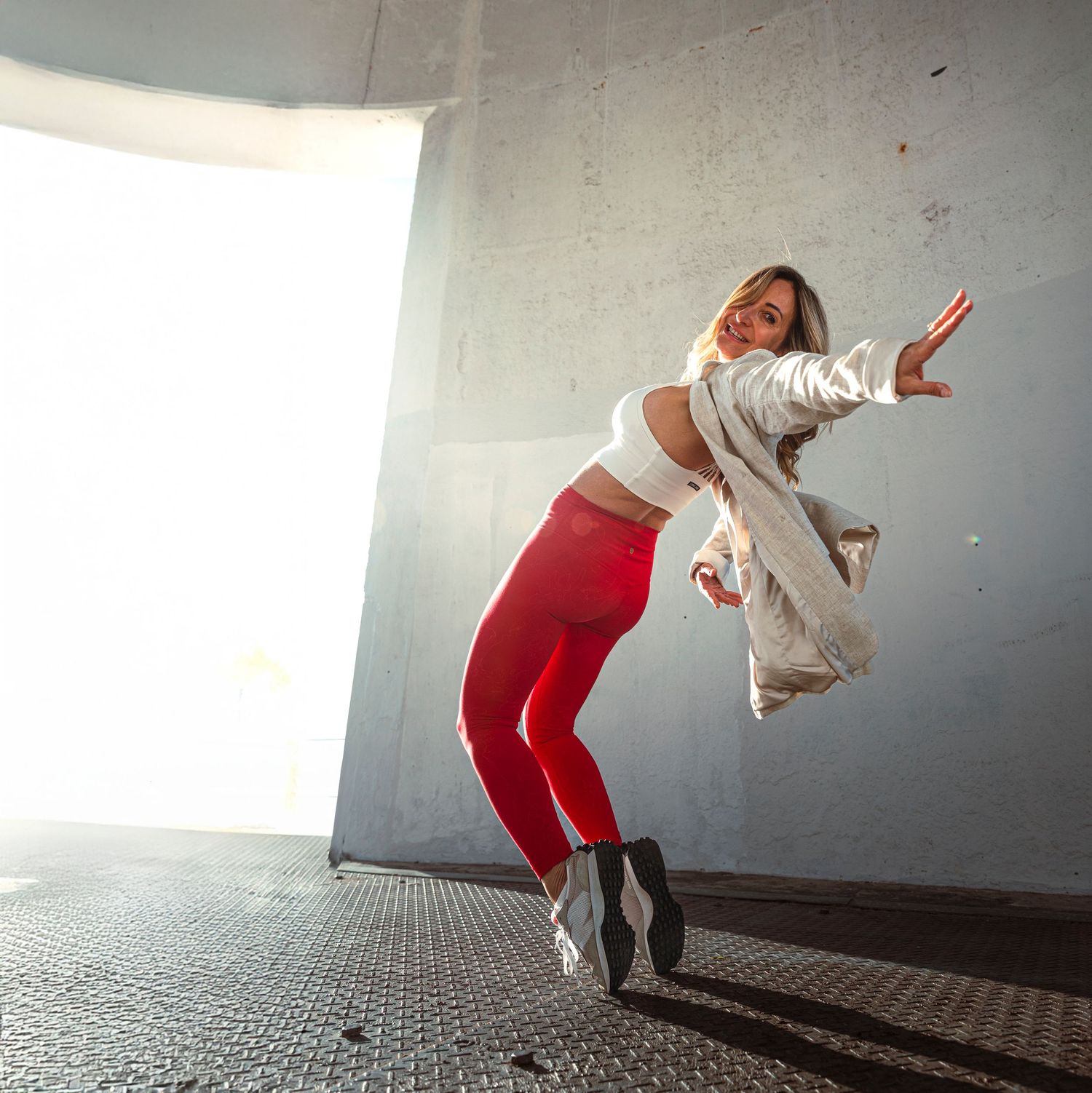 Woman in red leggings jumping dynamically in a concrete tunnel with bright backlight.