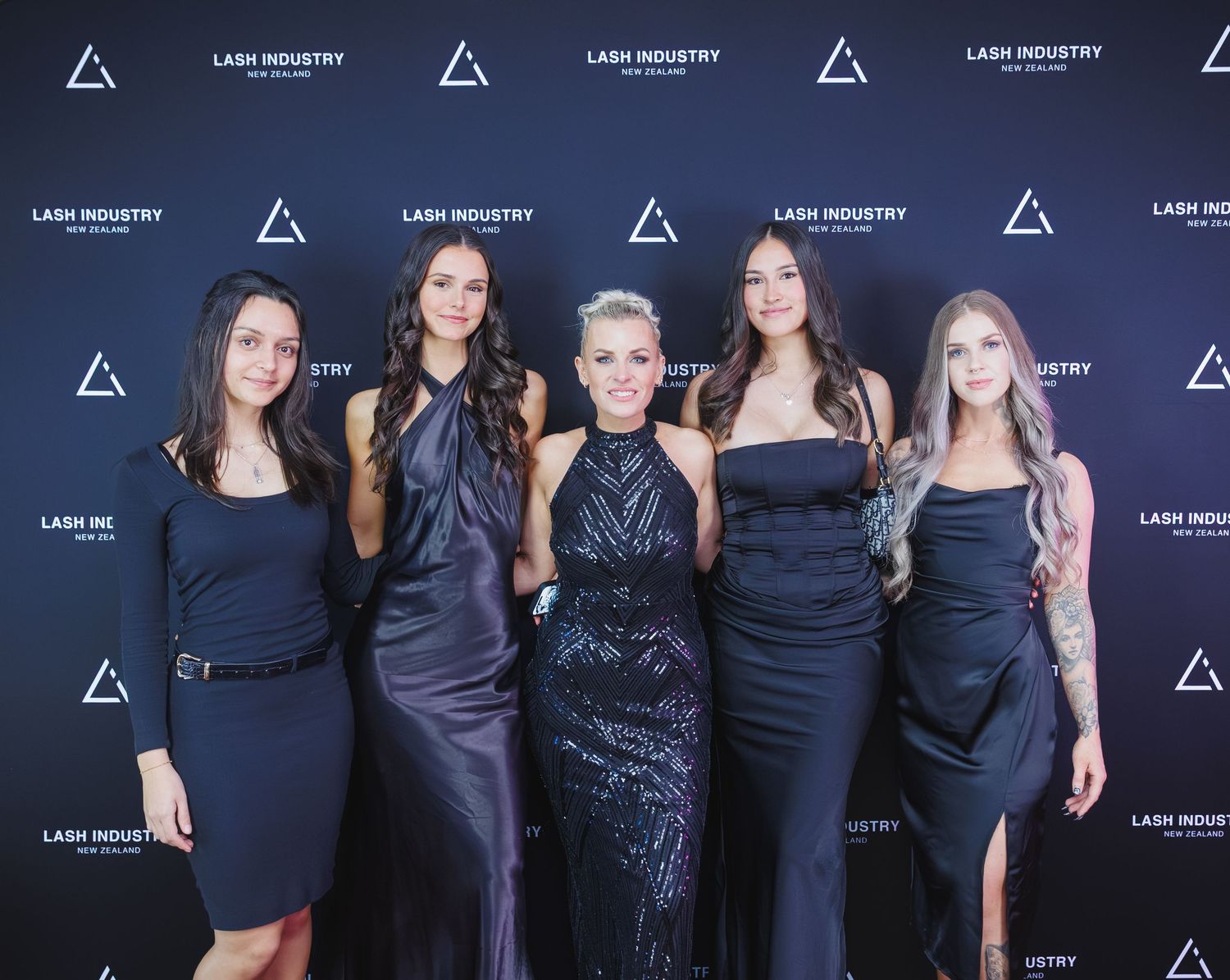 Five women in black formal wear posing at Lash Industry New Zealand awards backdrop.