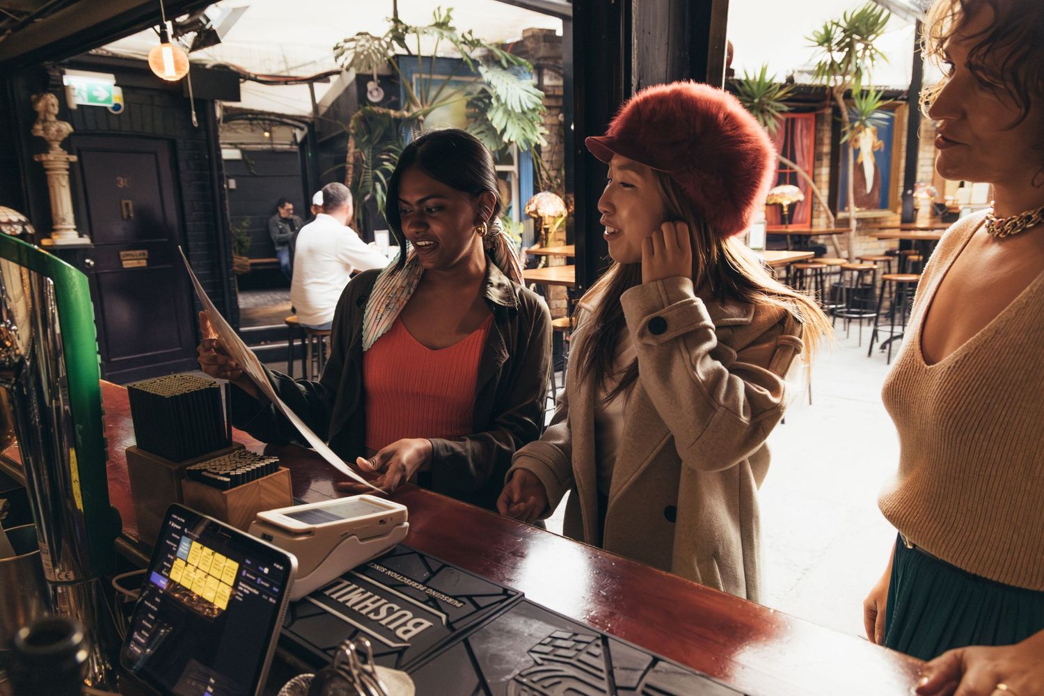 Two women smiling at a bar counter while a bartender assists them in a cozy pub setting.