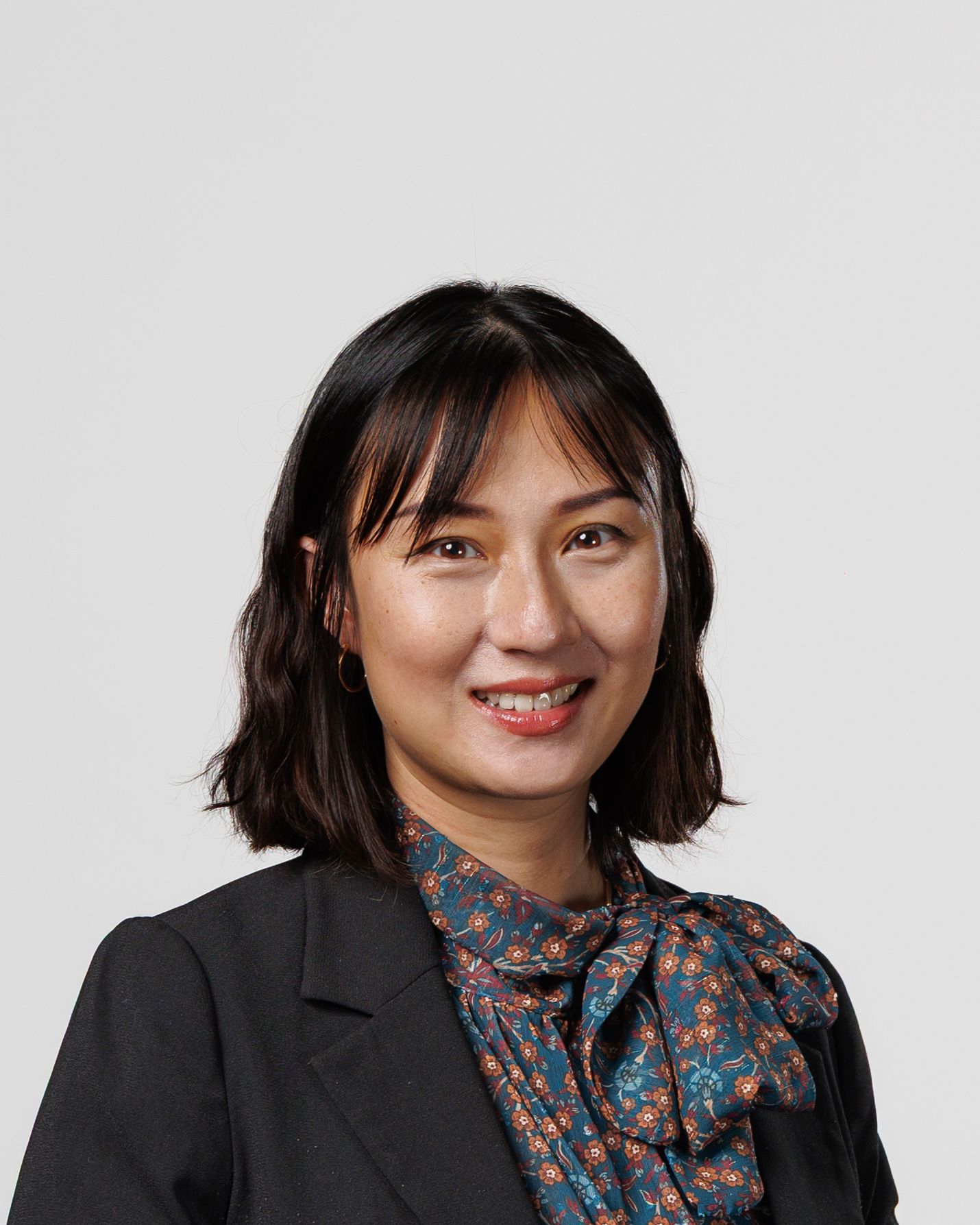 Professional headshot of a smiling woman with dark hair wearing a floral blouse and black blazer.