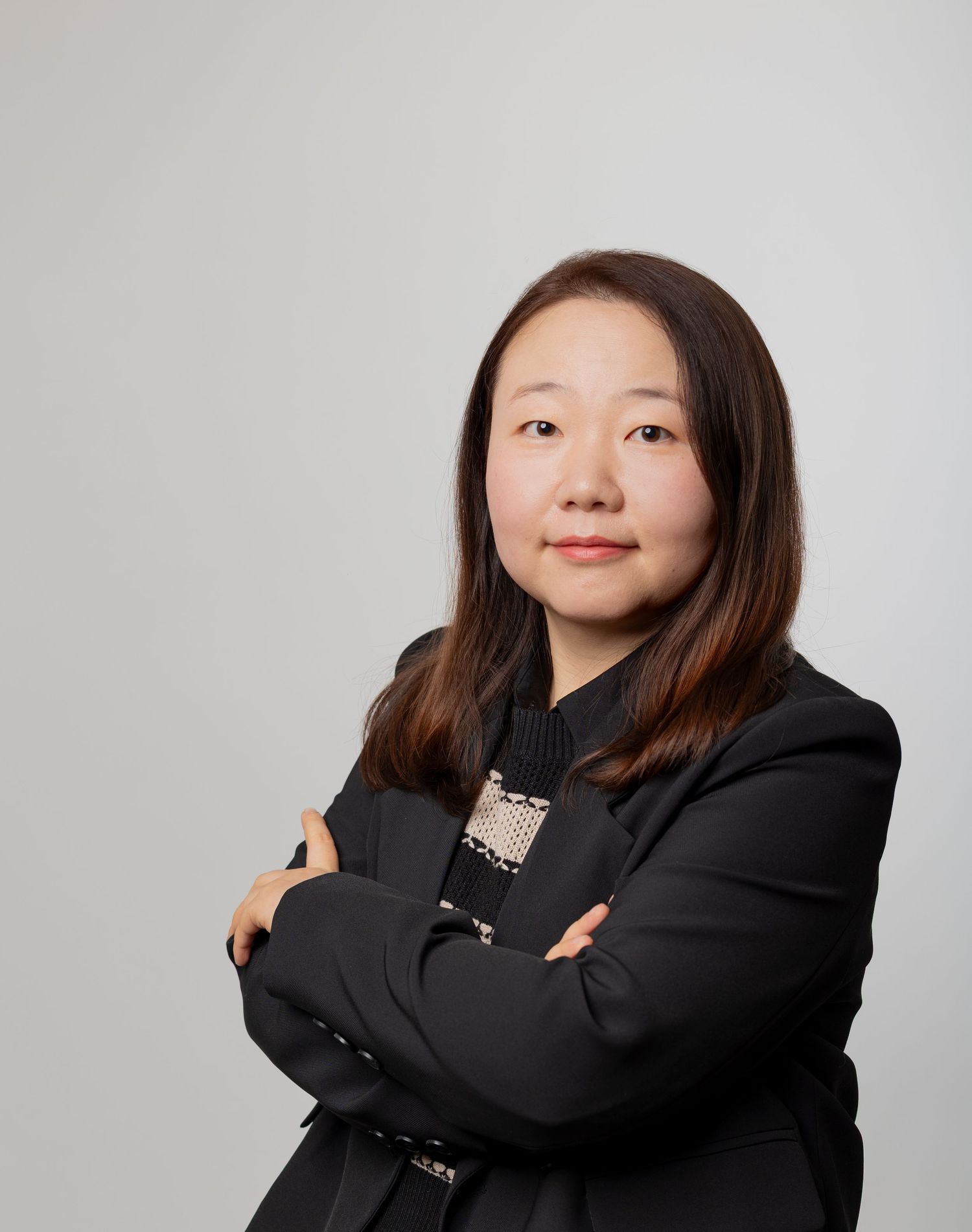 Professional headshot of a young Asian woman with long dark hair wearing a black blazer with arms crossed.