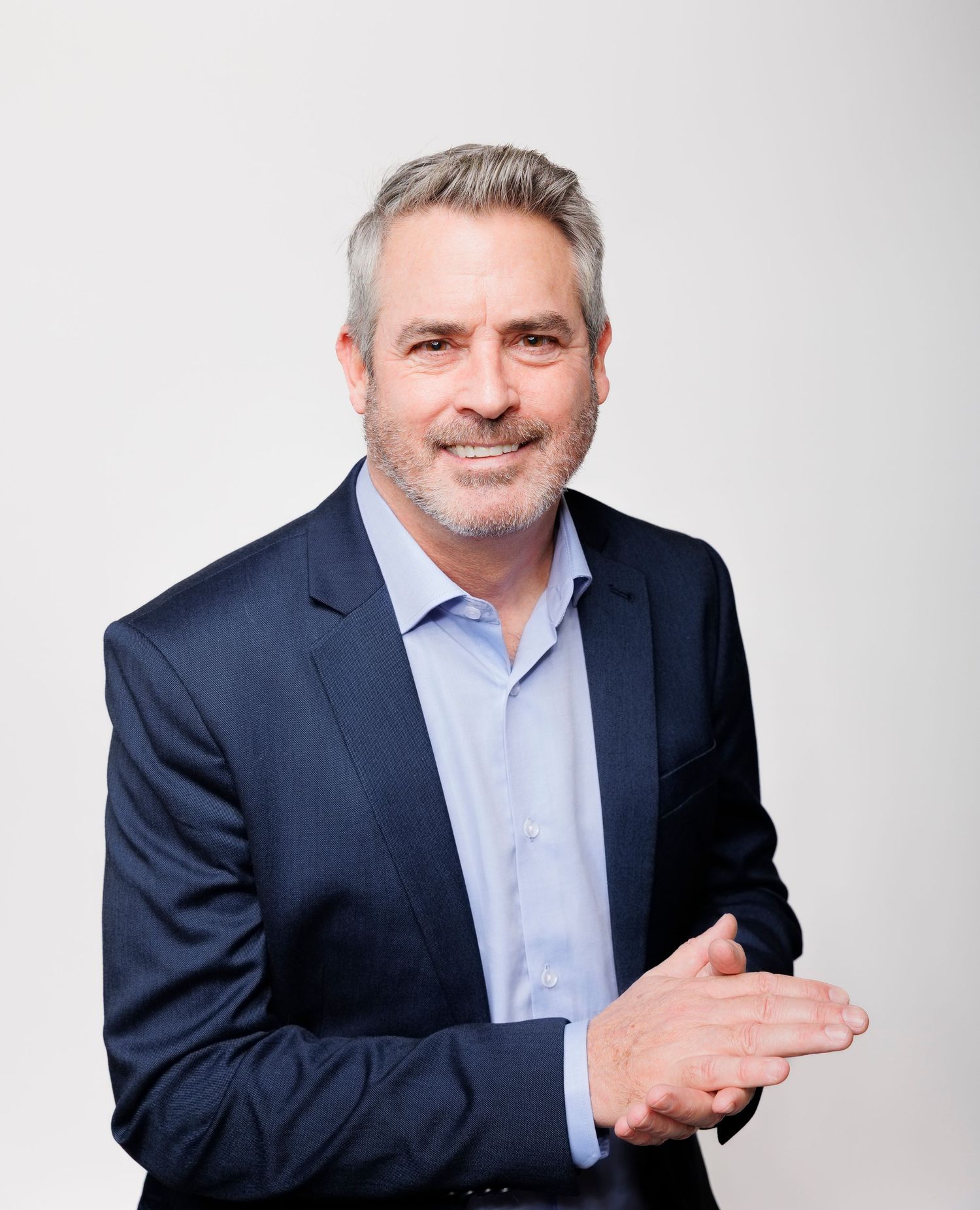 Professional headshot of a middle-aged man with gray hair and beard wearing a navy blazer and light blue shirt.