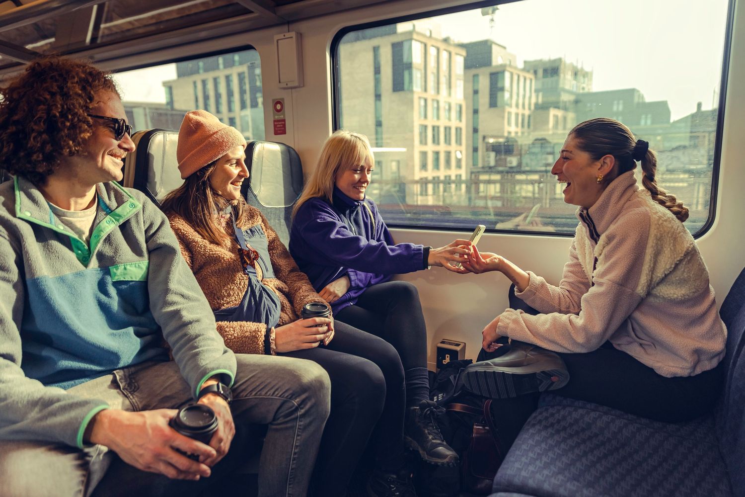 Group of four smiling friends enjoying a conversation while traveling on a train.