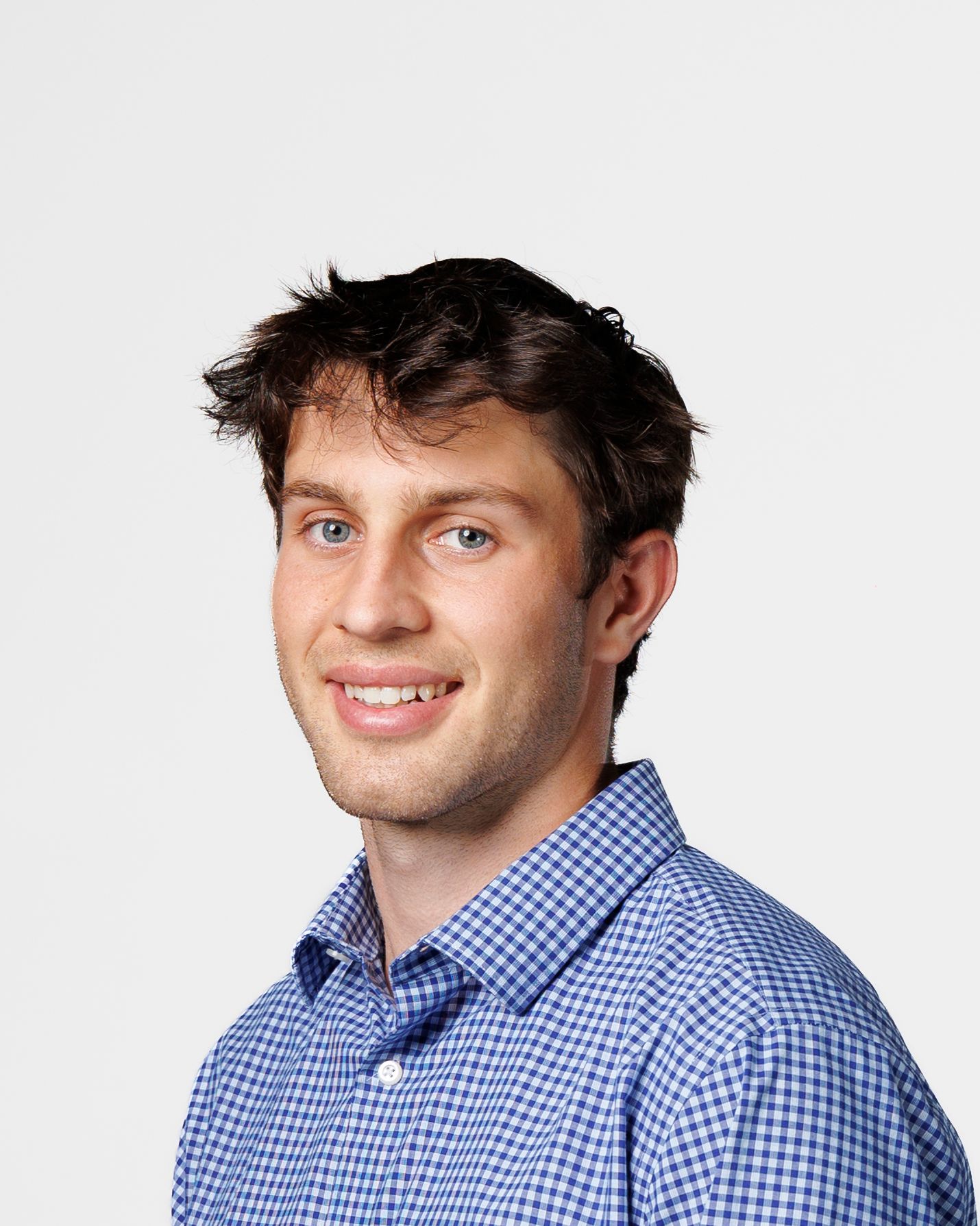 Young professional man smiling in blue checkered shirt against white background, headshot portrait photo.