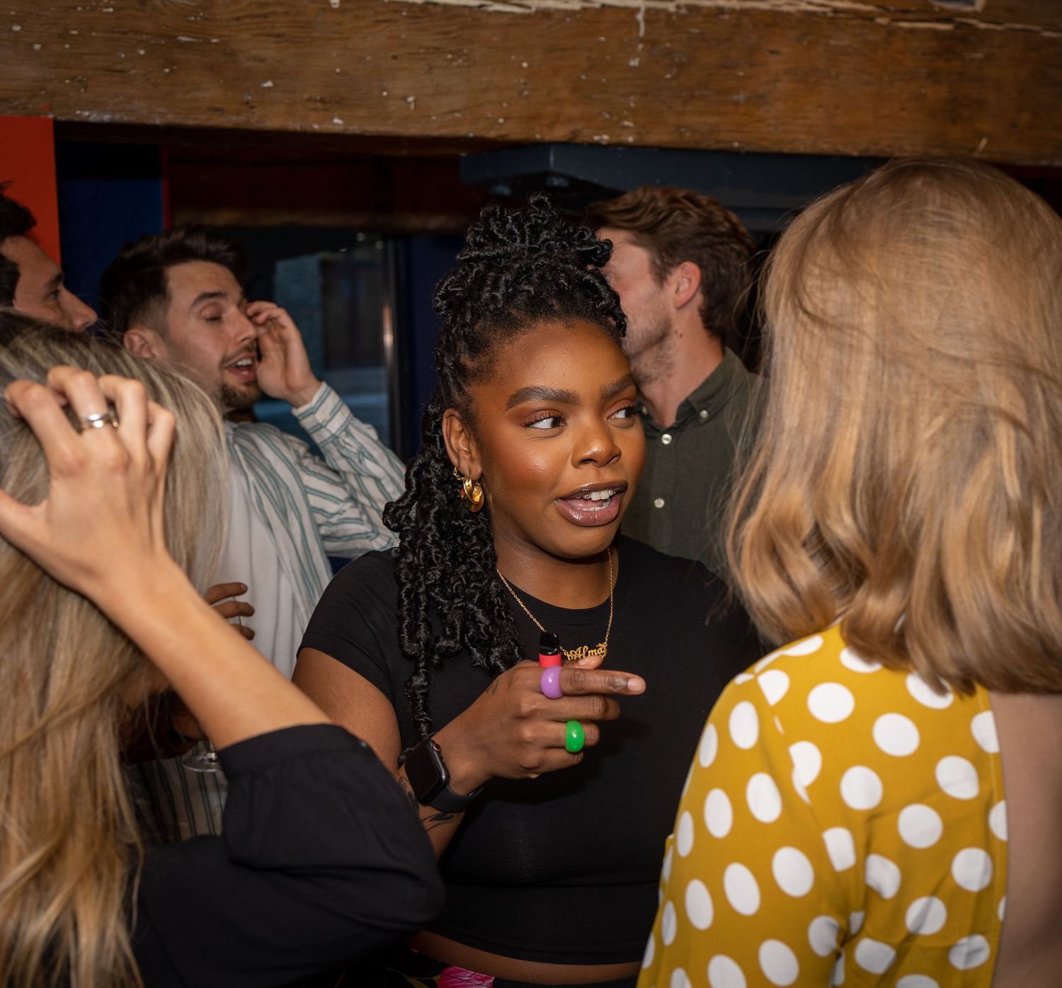 Young woman with braids chats animatedly with friends at a lively social event.
