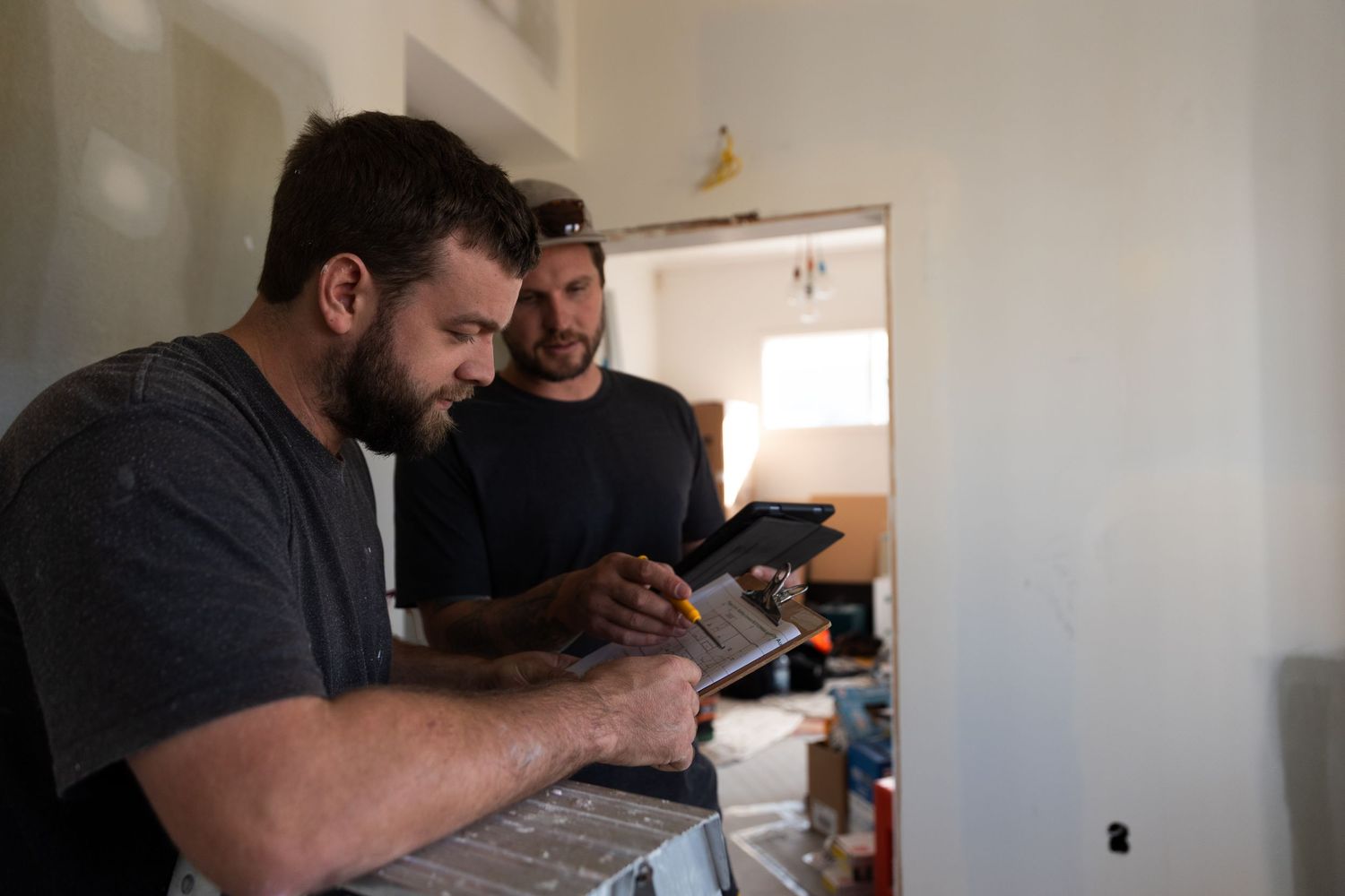 Two construction workers collaborating over a tablet and laptop inside a renovation site.
