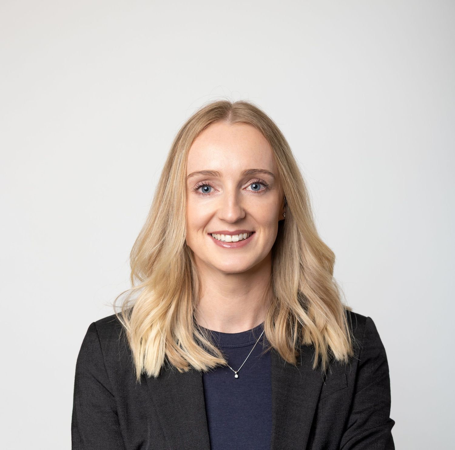 Professional headshot of a young blonde woman with shoulder-length hair wearing a dark blazer and navy top.