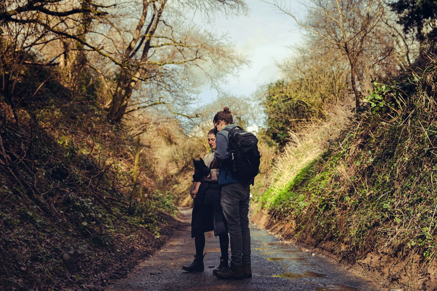 Two hikers consulting a map on a quiet tree-lined country lane.