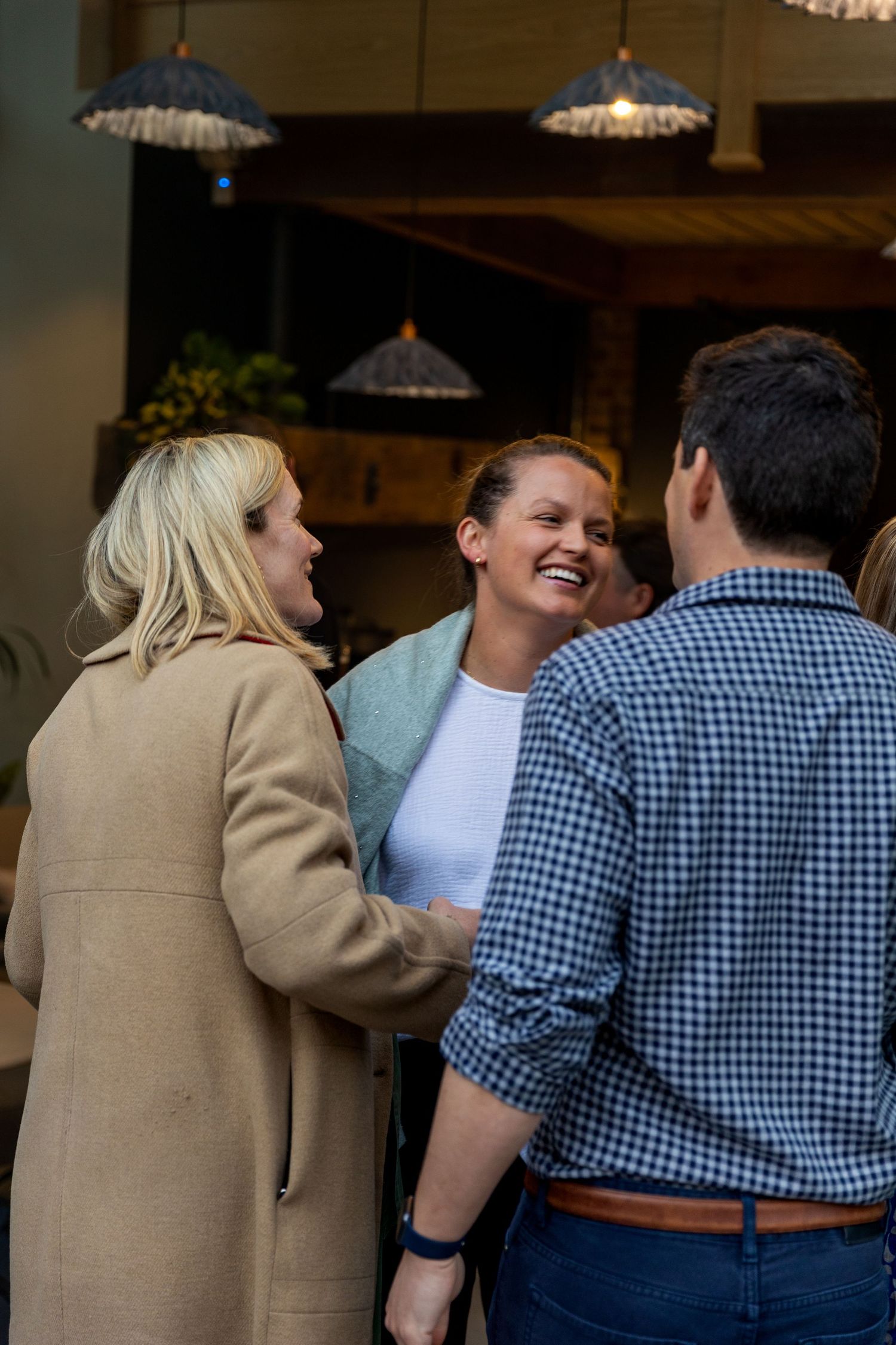 Three people laughing and socializing at an indoor networking event in a warmly lit venue.