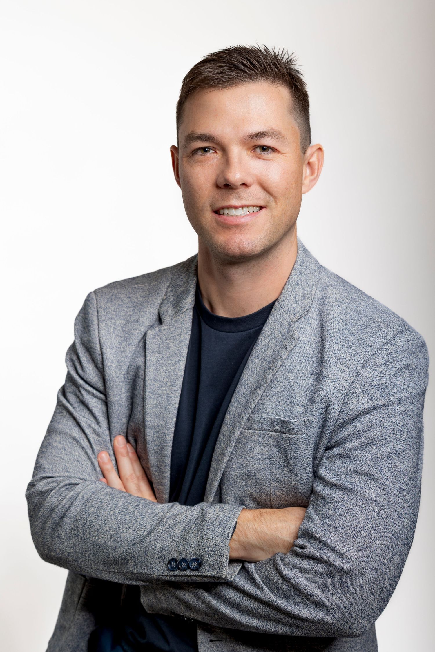 Man in grey blazer with arms crossed looking at the camera with a nice smile