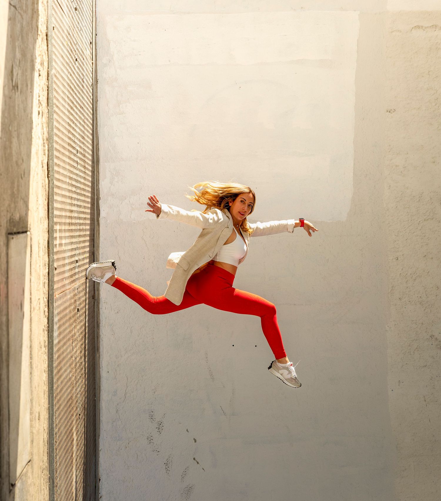 Athletic woman in red leggings leaping dynamically against white urban wall.