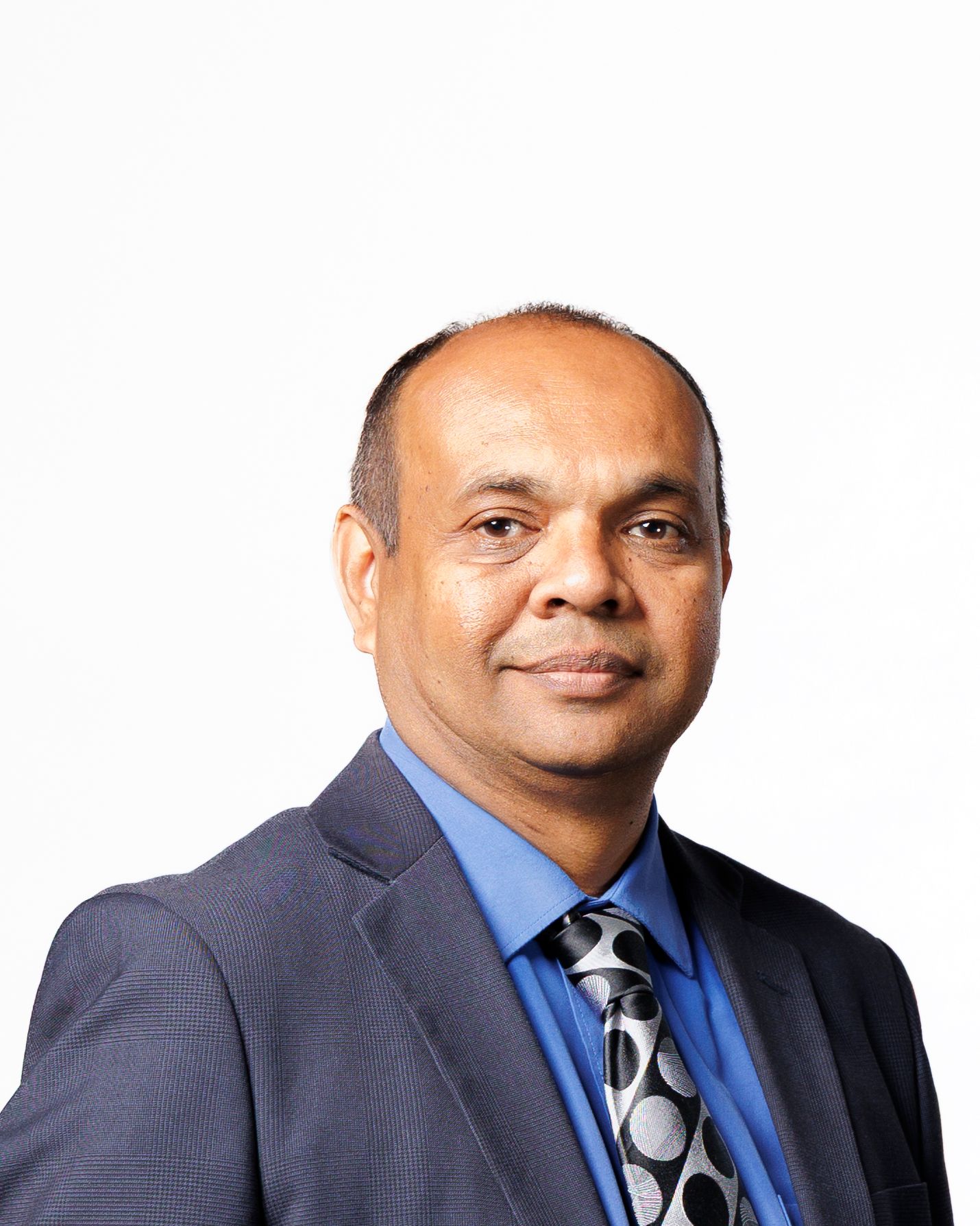 Professional headshot of a man in a blue shirt, gray blazer, and patterned tie against a white background.