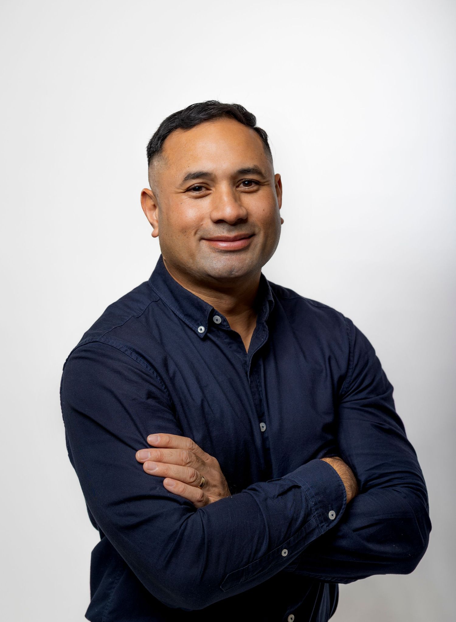 Confident man in dark navy shirt standing with arms crossed against a white background.