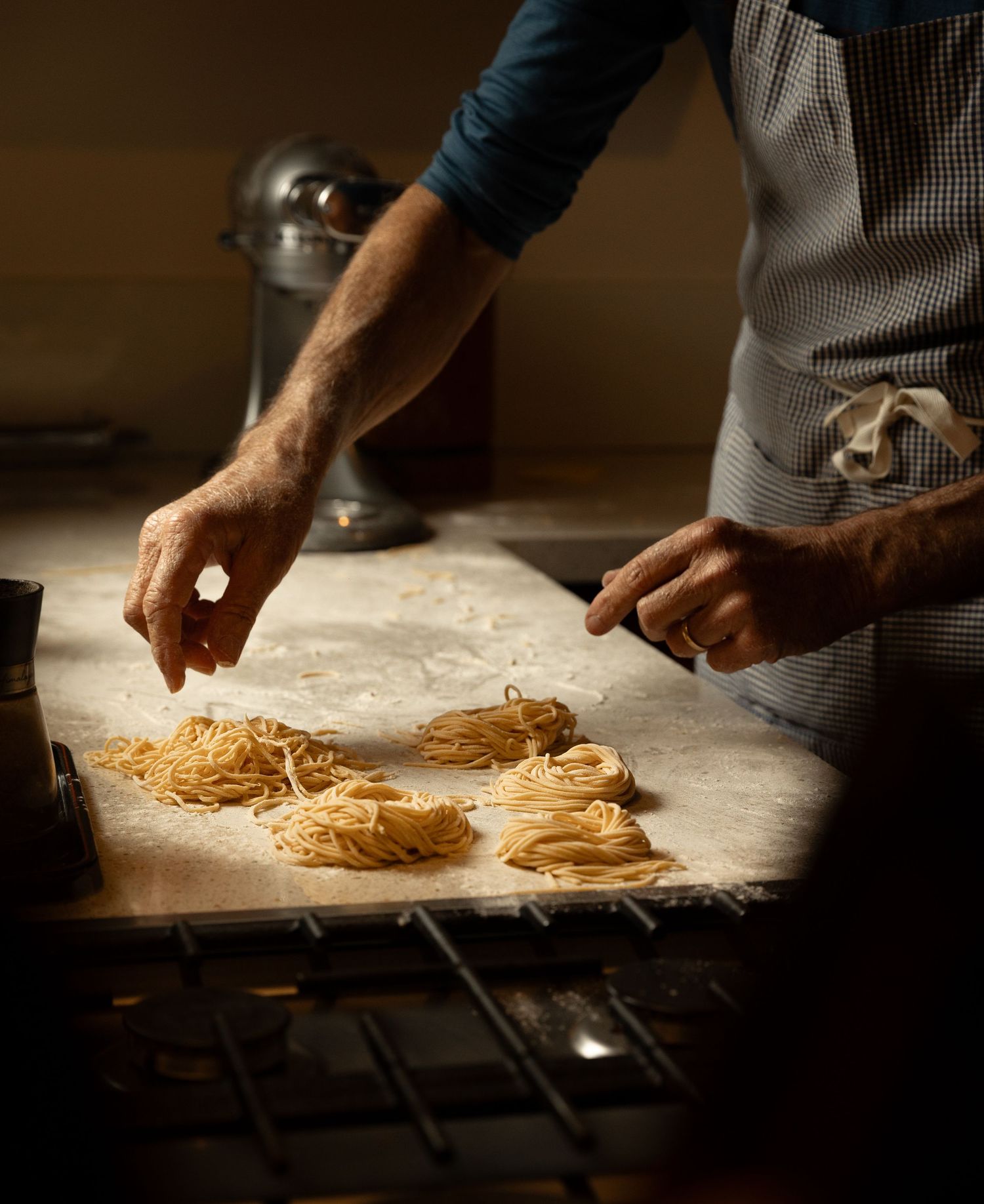 Chef sprinkling flour on fresh homemade pasta nests on a floured surface in a rustic kitchen.