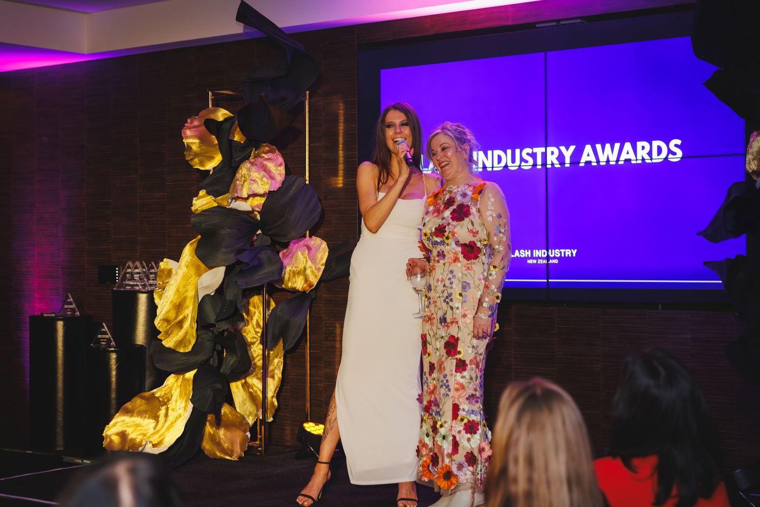 Three presenters on stage at the Lash Industry Awards ceremony with purple lighting.