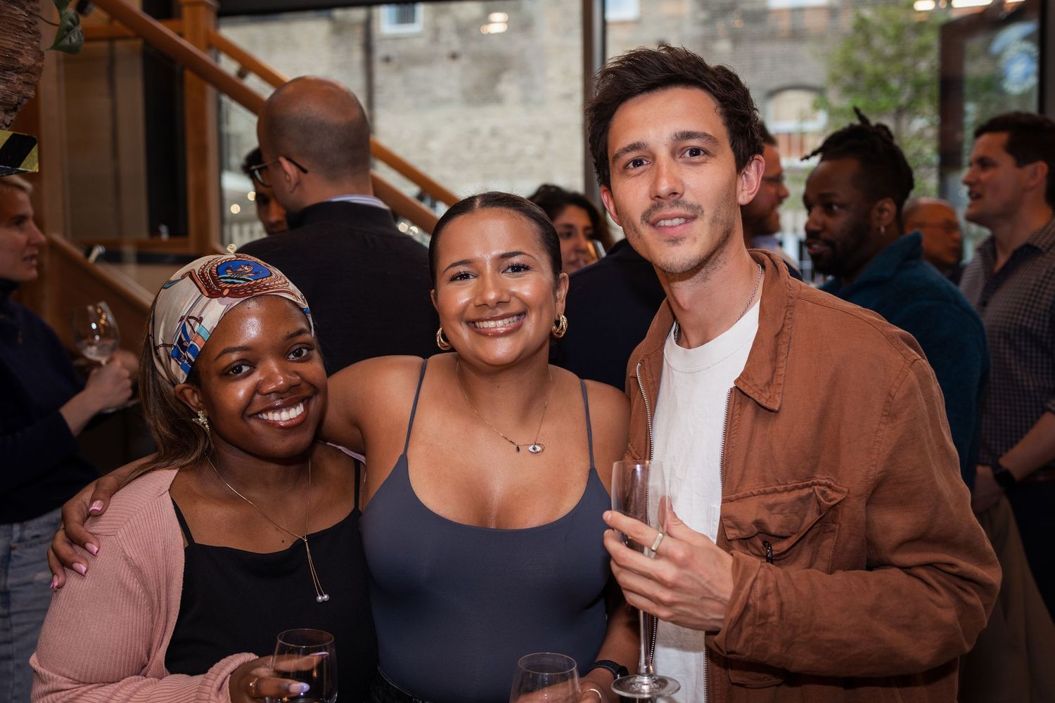 Two women and a man smile together for a photo while holding drinks at a social event.